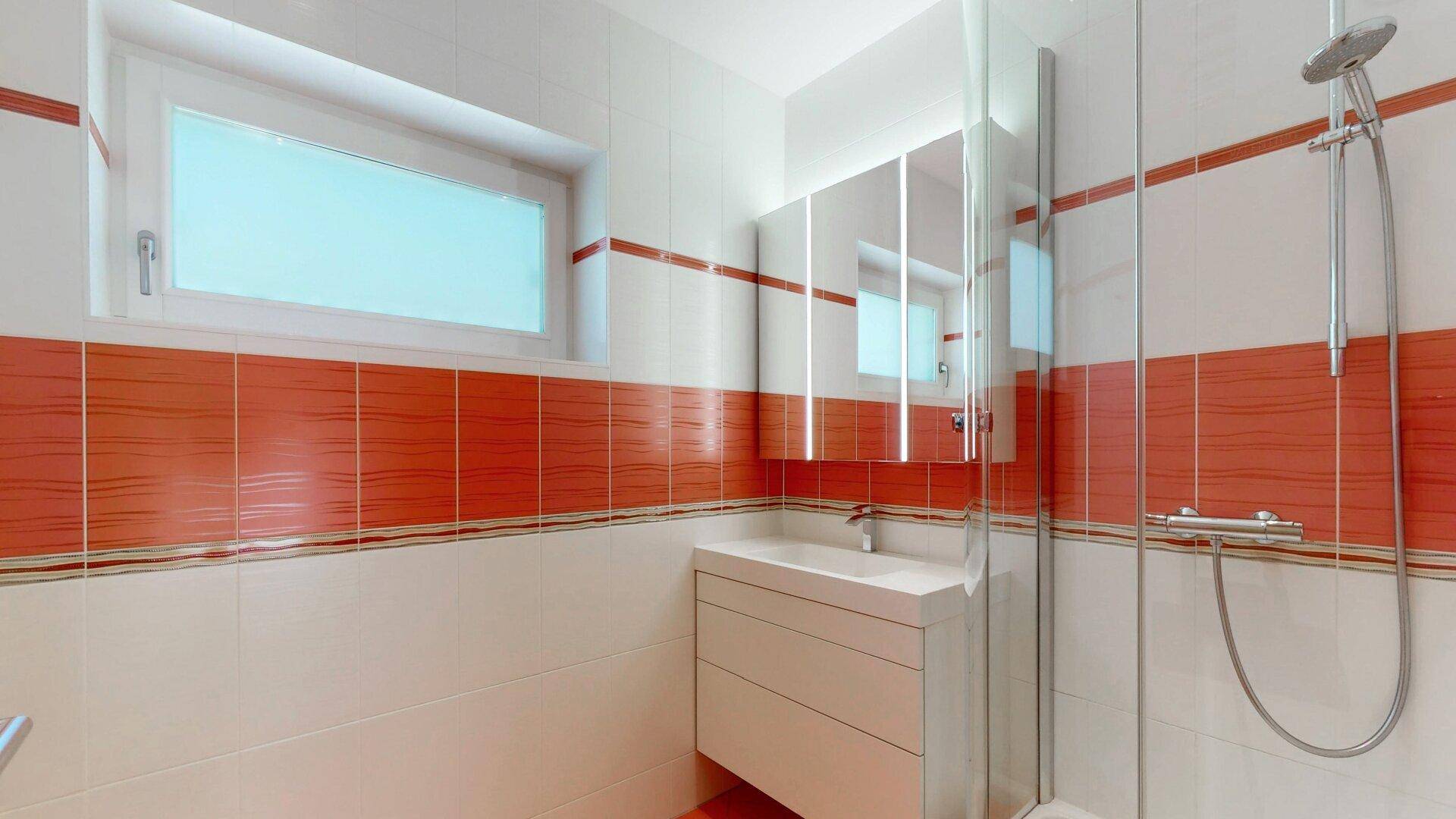 Modernes Badezimmer mit Dusche, Einzelwaschbecken und Fenster, in weiß-roter Farbgebung.
