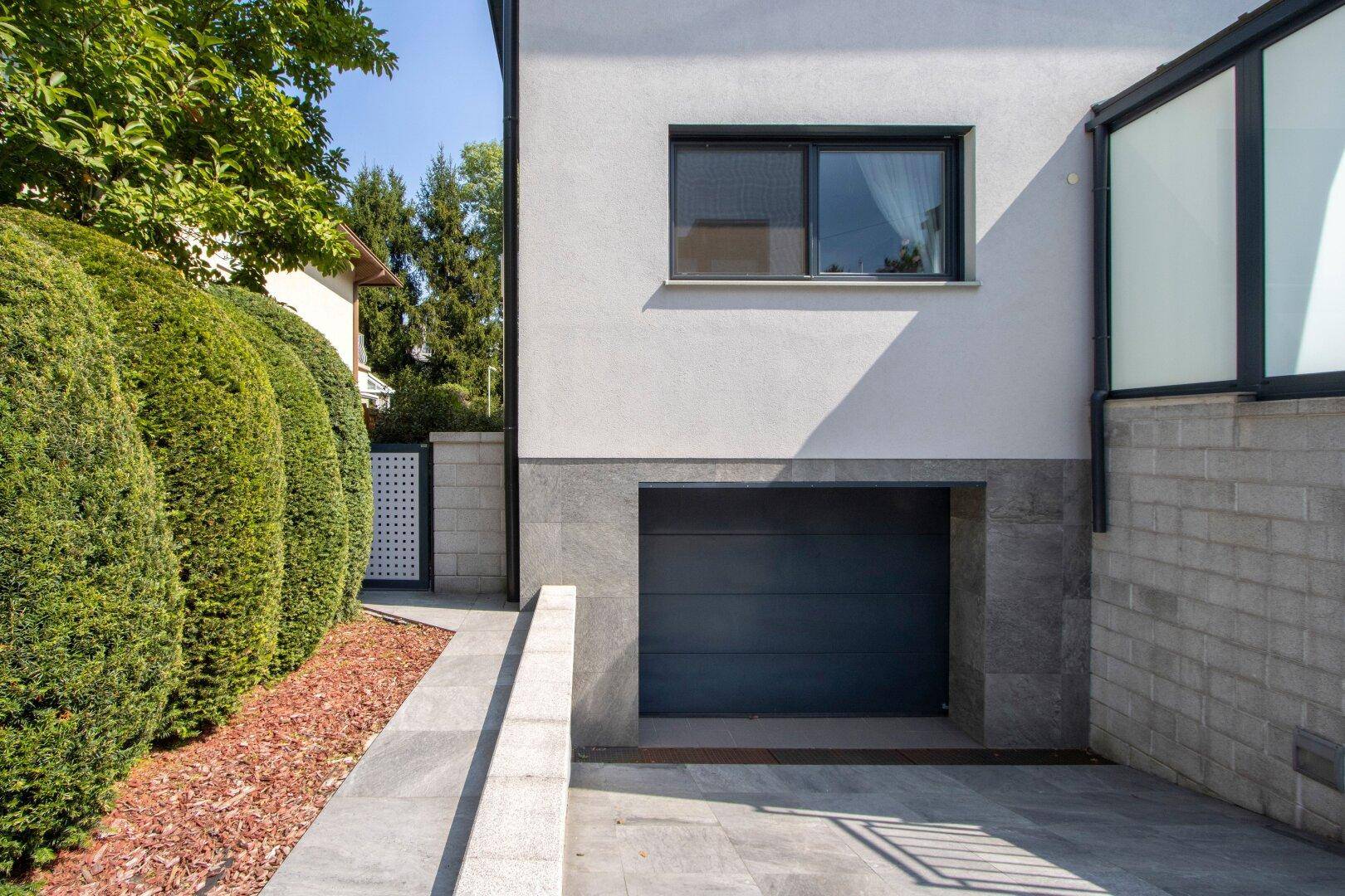 Außenansicht des Hauses mit integrierter Garage und gepflegter Hecke.