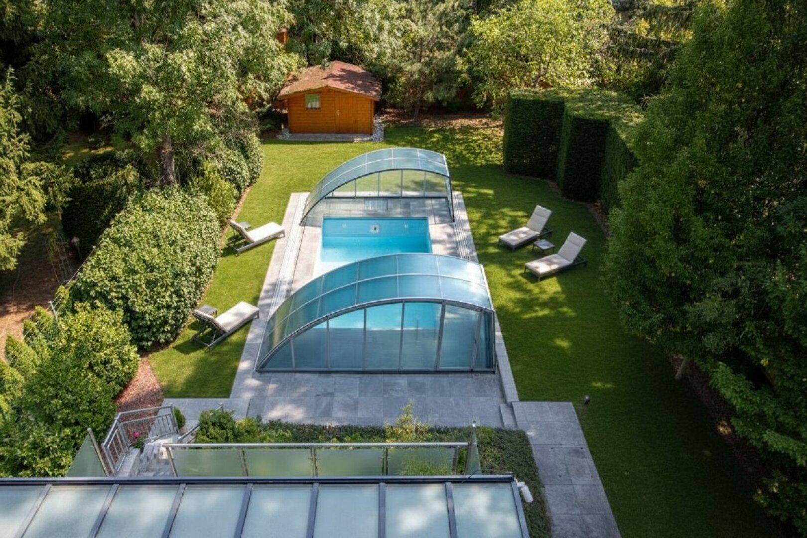 Vogelperspektive des Gartens mit zwei überdachten Pools, Liegestühlen und gepflegter Rasenfläche.