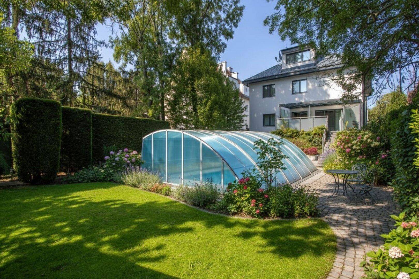 Großer Garten mit Rasenfläche, überdachtem Pool und Sitzbereich, umgeben von üppiger Vegetation.