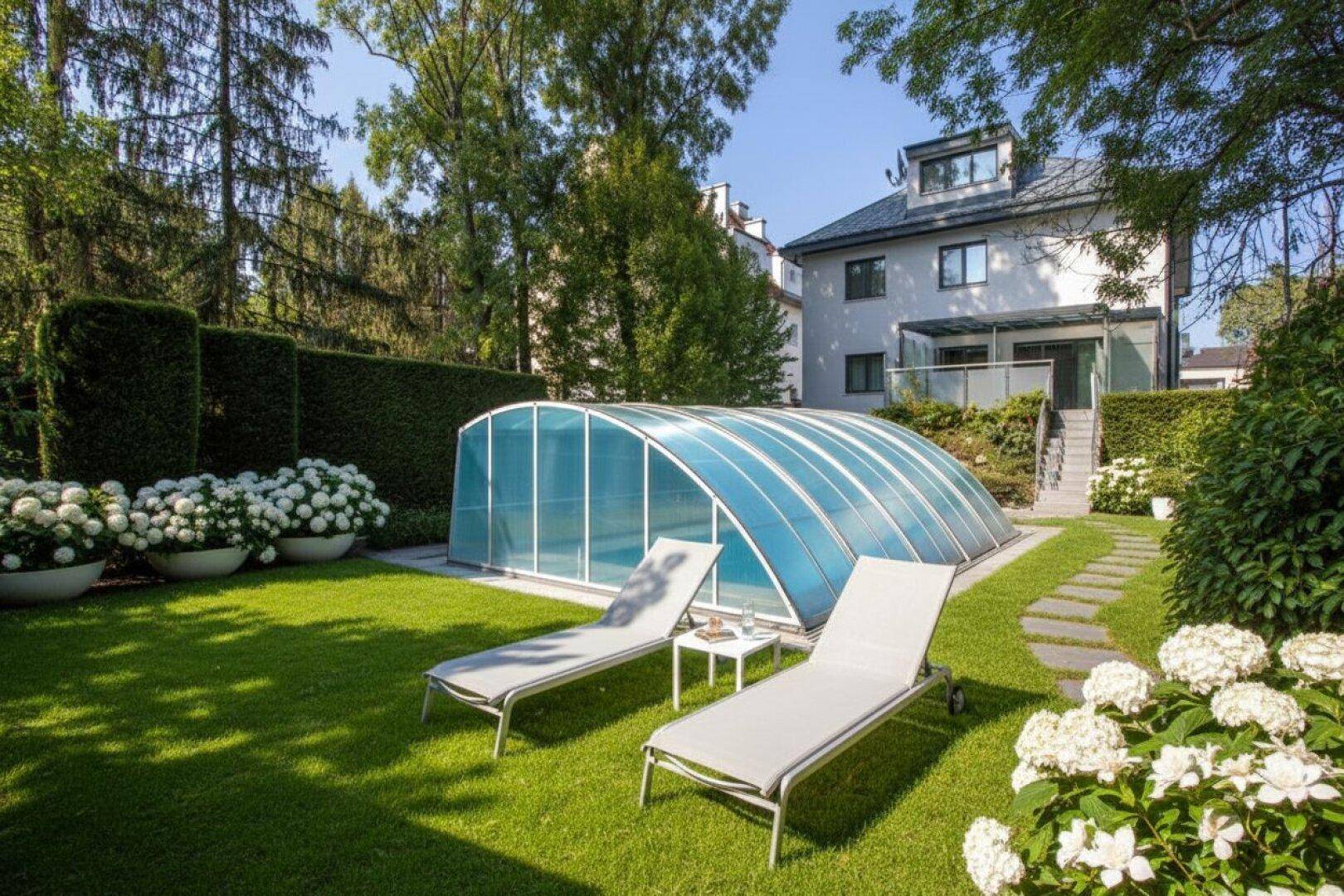 Großer Garten mit Rasenfläche, überdachtem Pool und Liegestühlen, umgeben von Bäumen und Hecken.