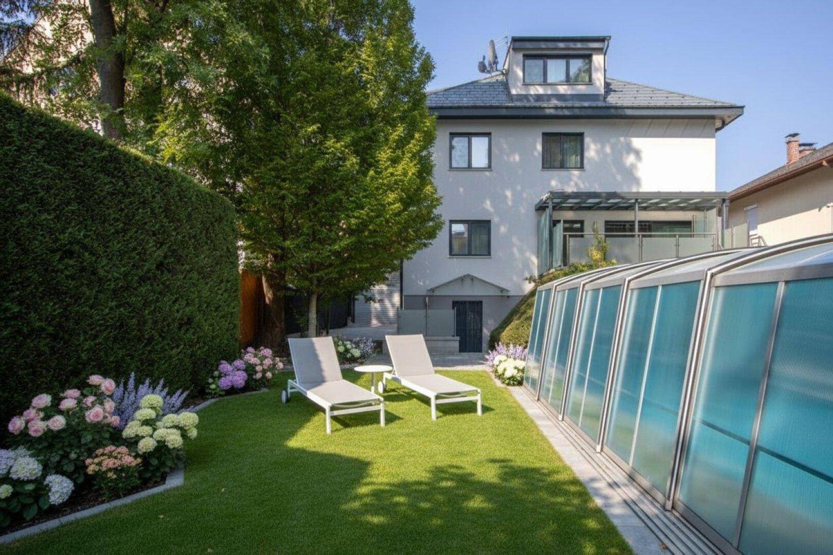 Gepflegter Garten mit Rasenfläche, überdachtem Pool und Liegestühlen, umgeben von Bäumen und Blumen.