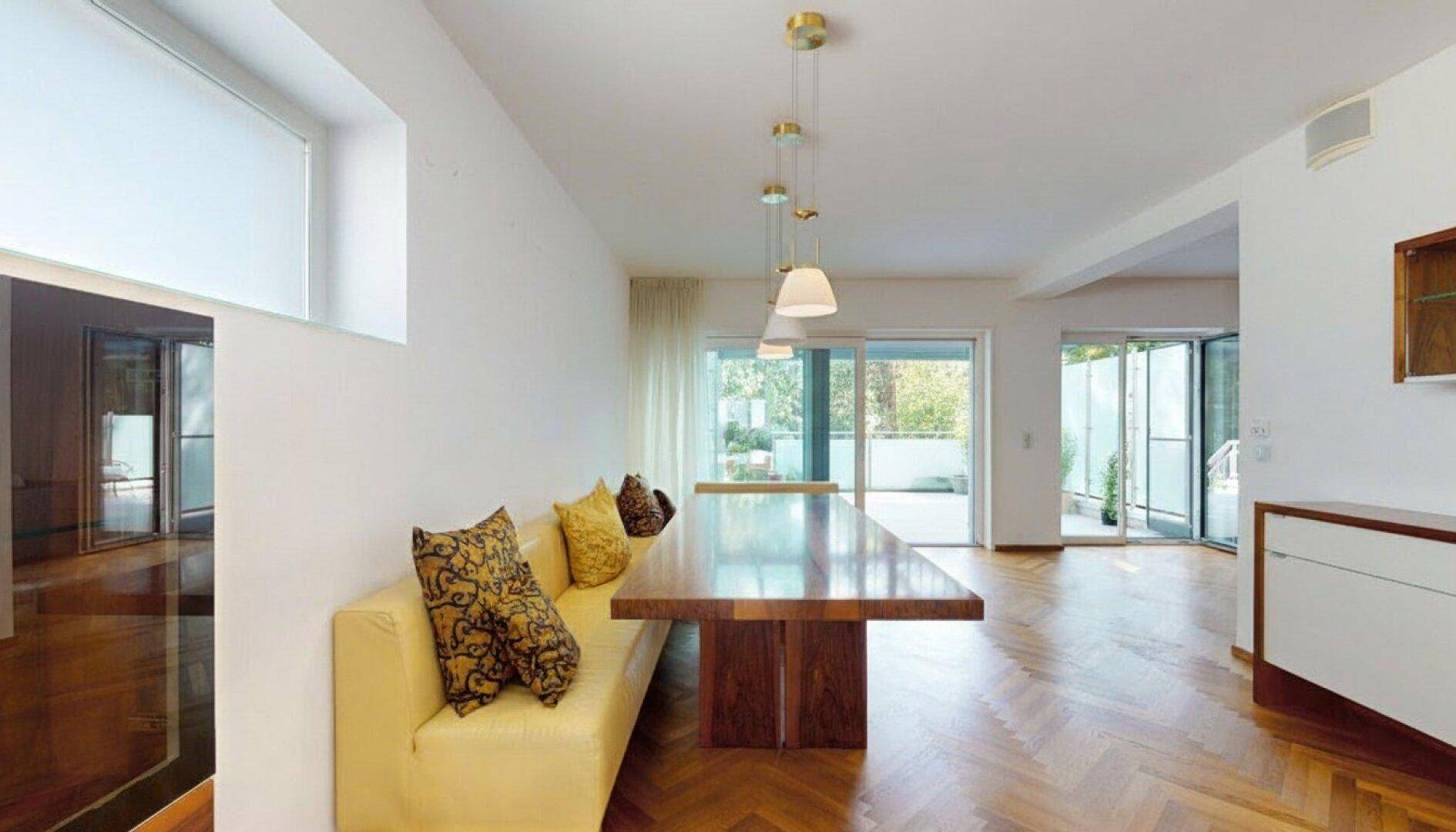 Eleganter Essbereich mit langem Holztisch, Sitzbank und Parkettboden, mit Zugang zur Terrasse.