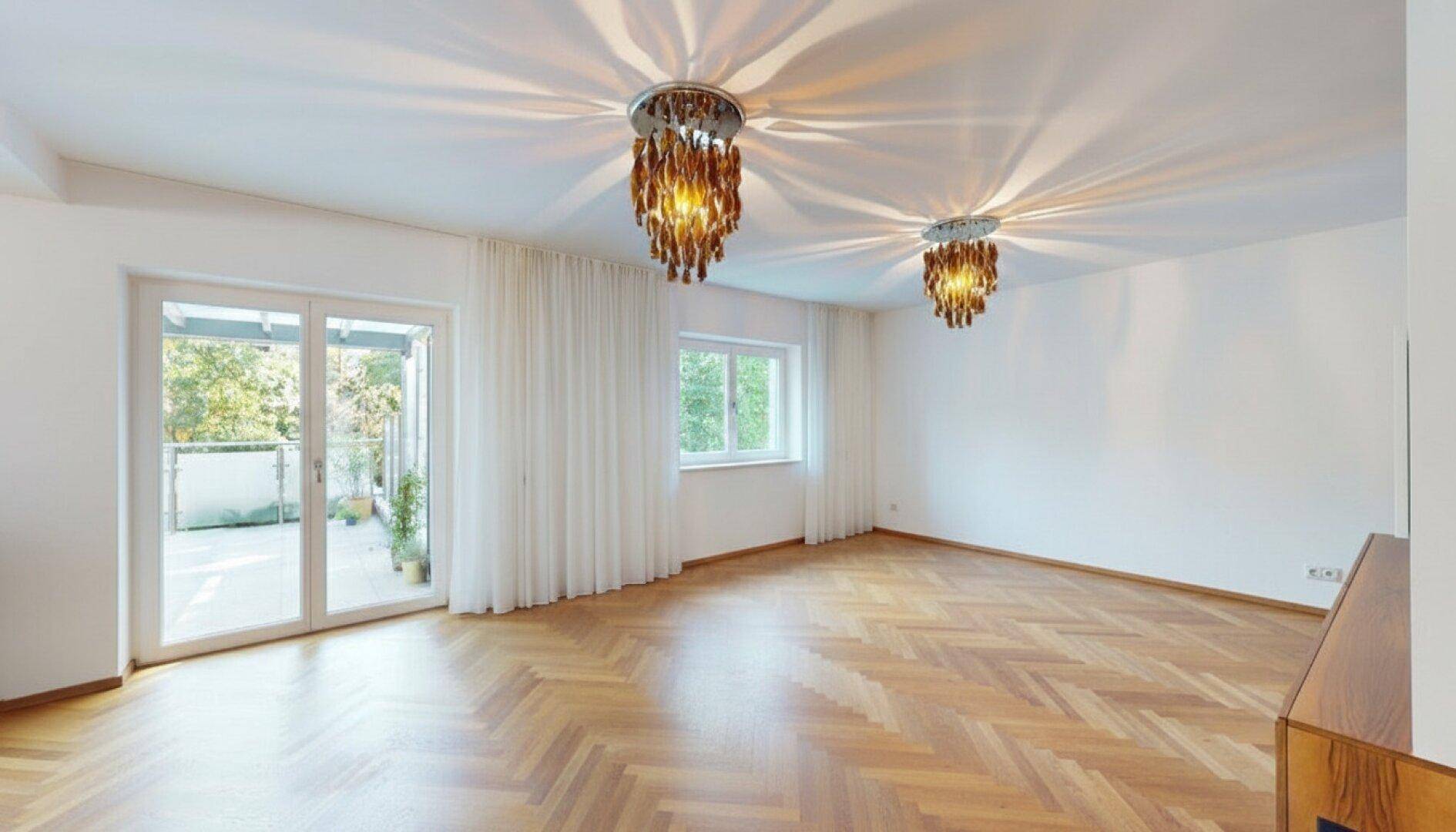 Geräumiges Wohnzimmer mit Fischgrätparkett, großen Fenstern und Balkonzugang, bereit zur individuellen Gestaltung.