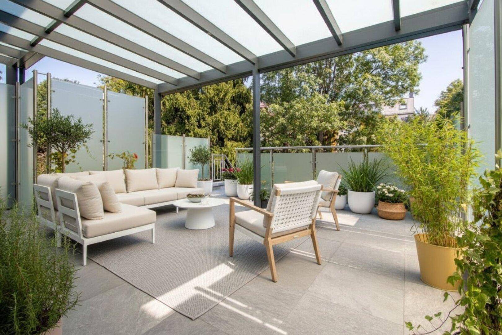 Überdachte Terrasse mit modernen Loungemöbeln, Steinboden und Glasabtrennungen für Privatsphäre.