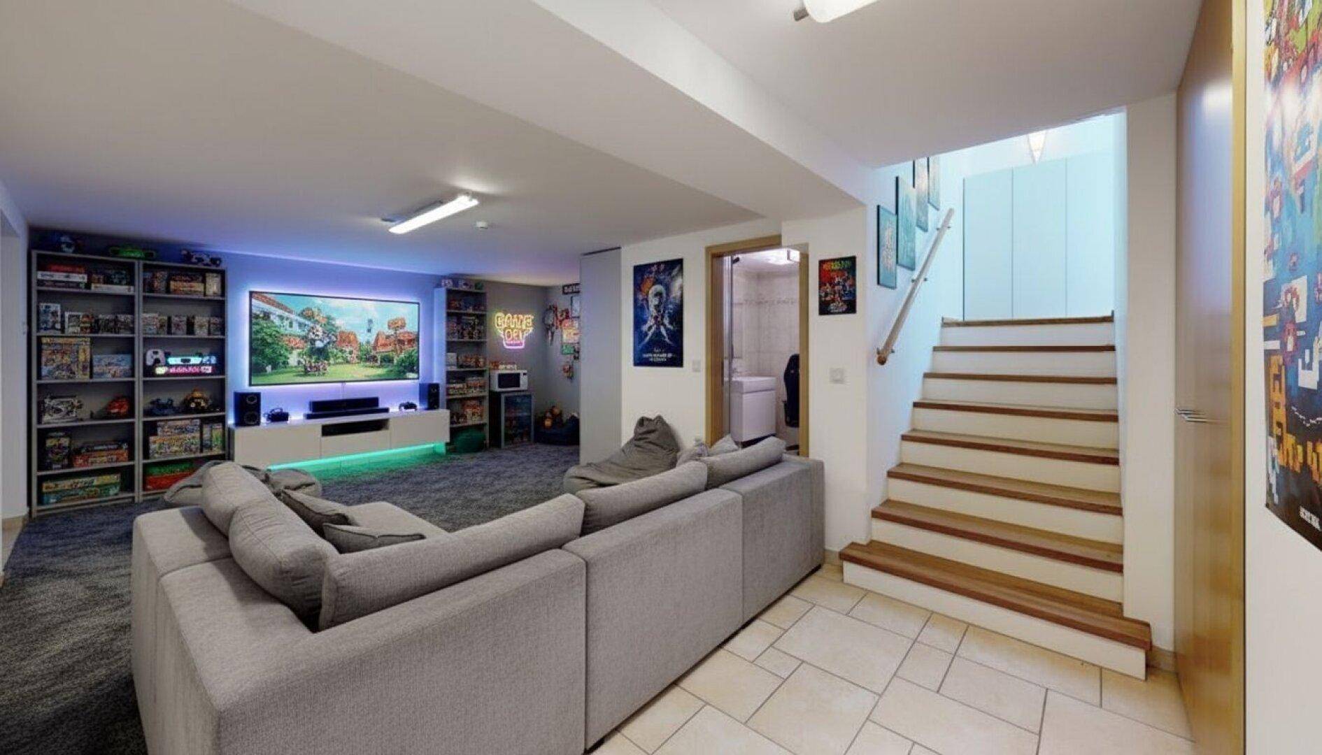 Unterhaltungsbereich im Keller mit großem Sofa, Fernseher und Regalen für Spiele und Medien.