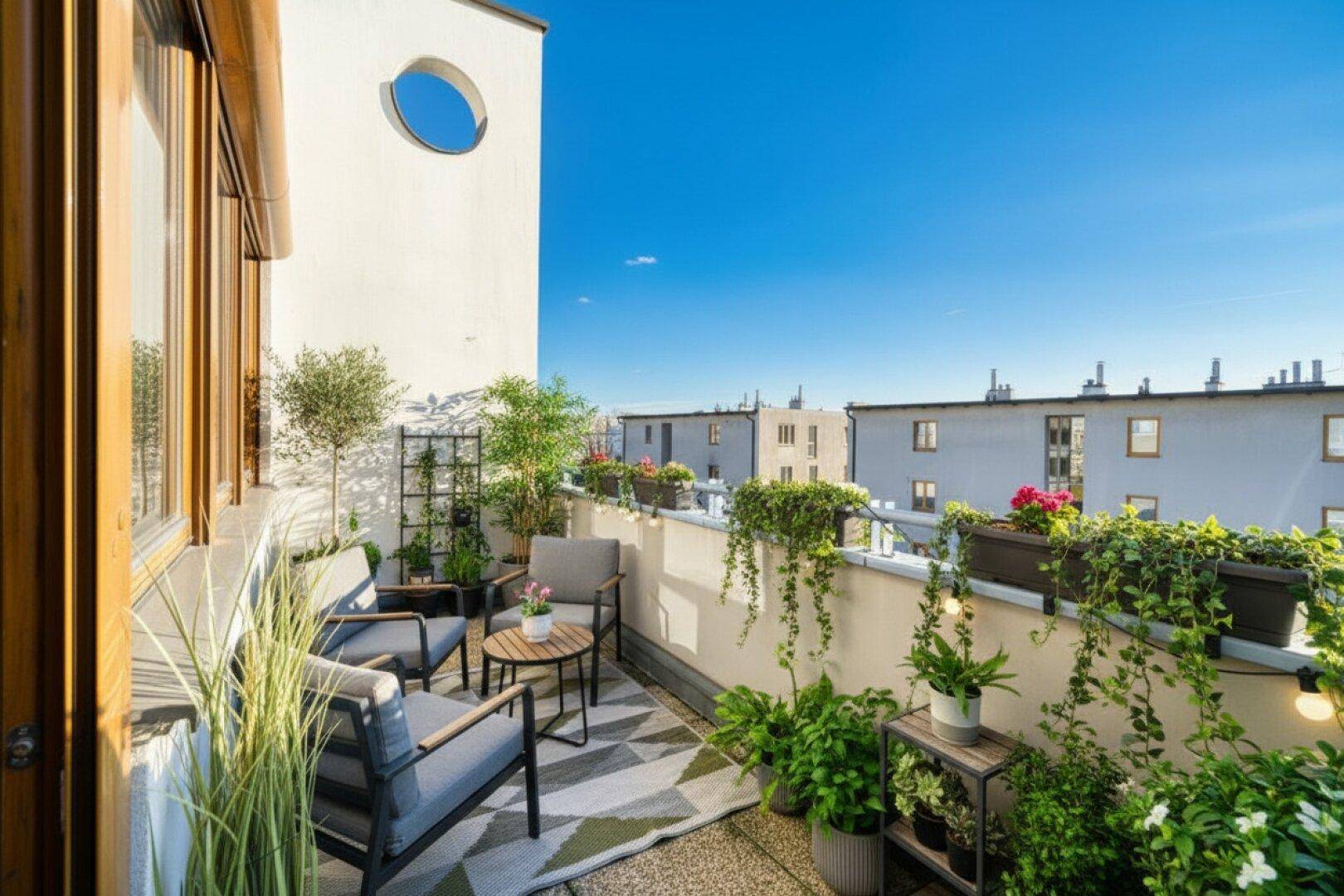 Gemütlicher Balkon mit Sitzgelegenheiten, vielen Pflanzen und Blick auf die Nachbarschaft.