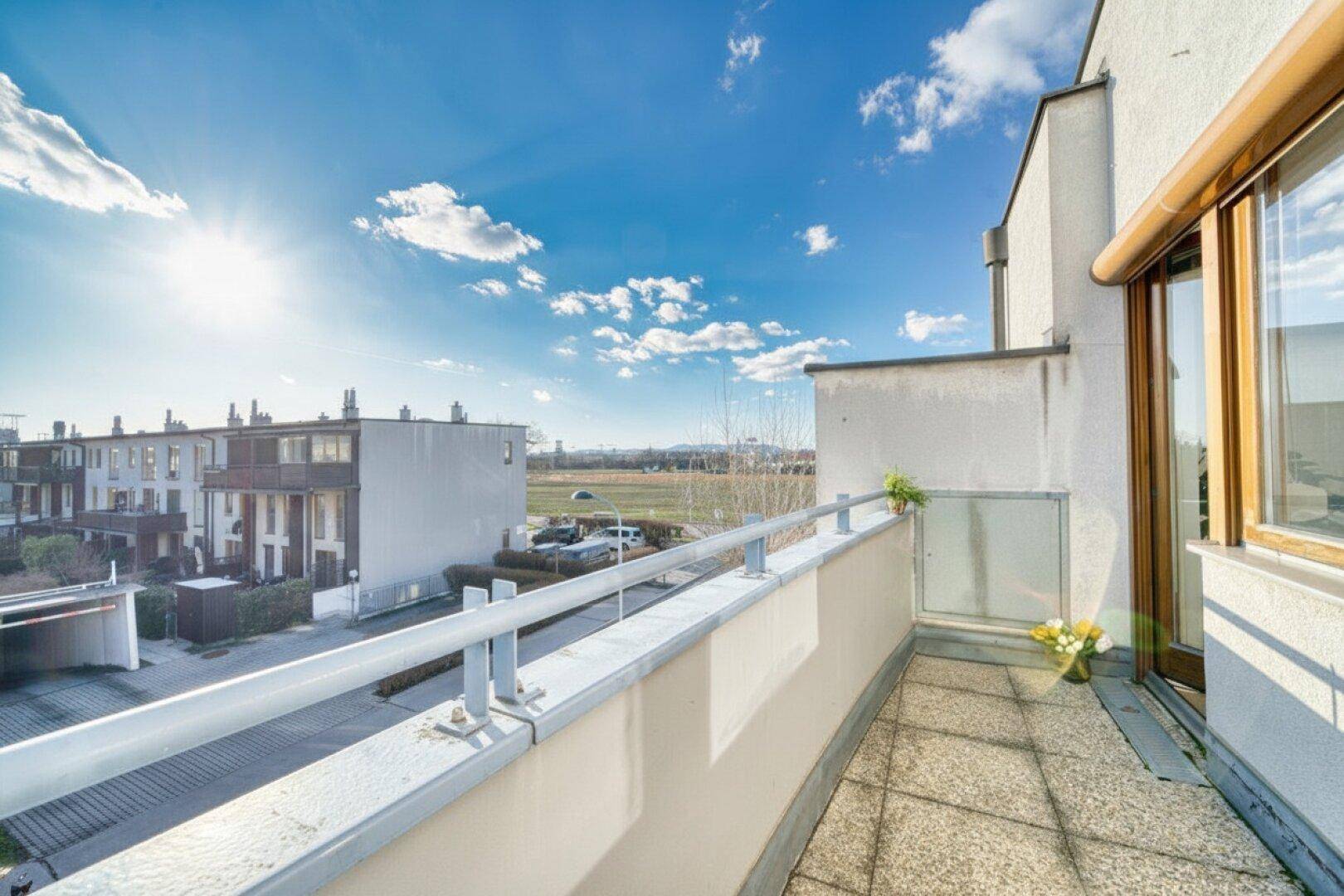 Sonniger Balkon mit Fliesenboden und weitem Blick über die Umgebung und grüne Flächen.