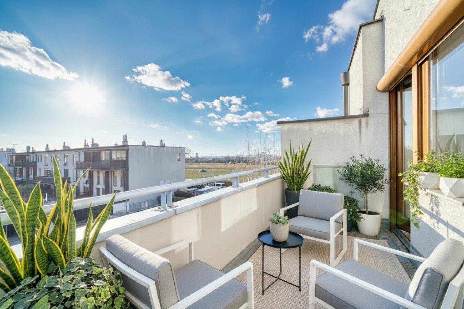 Heller Balkon mit modernen Sitzmöbeln, Pflanzen und weitem Blick in die sonnige Landschaft.