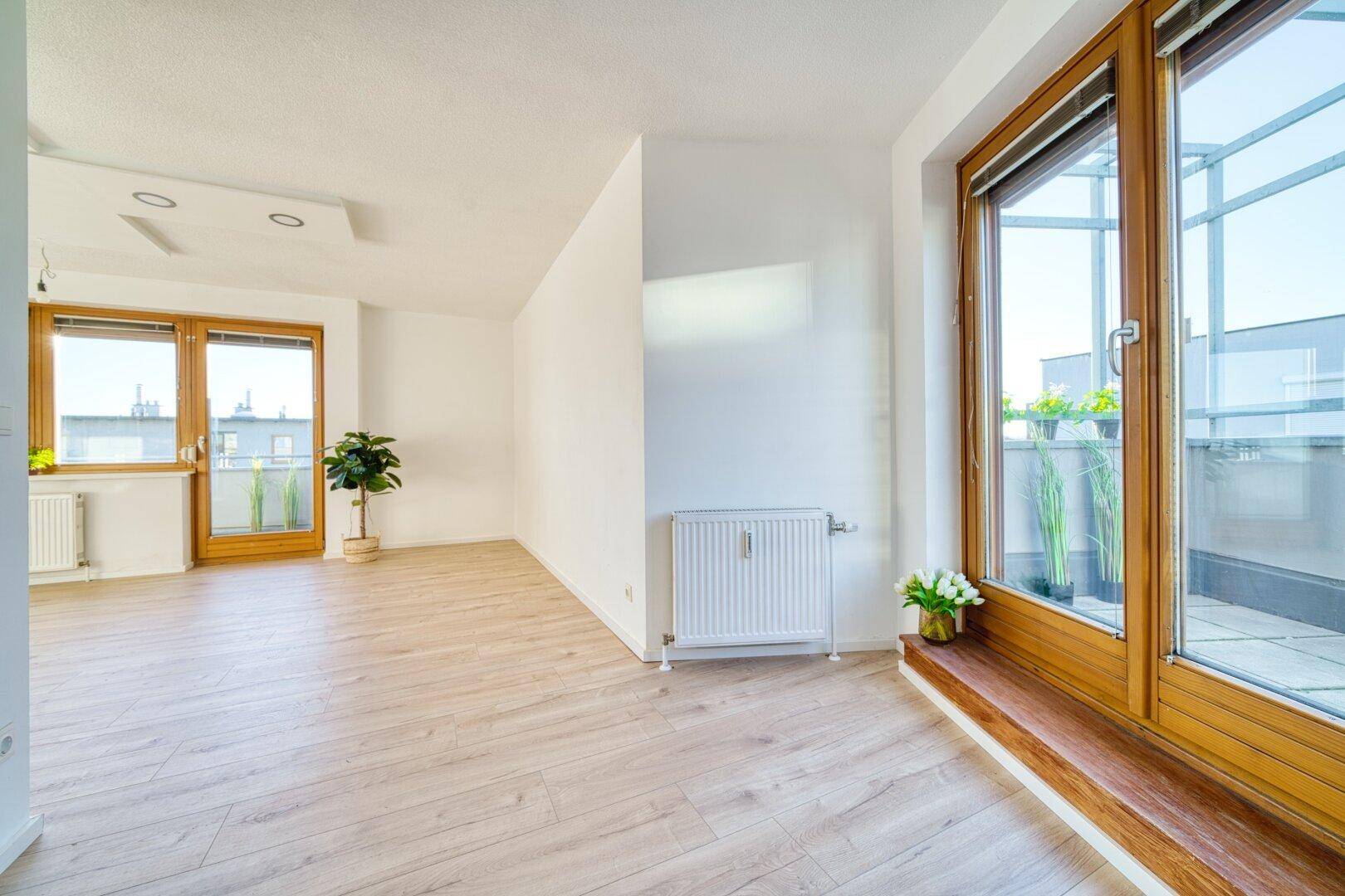 Heller, leerer Wohnbereich mit großen Fenstern und Zugang zu einem Außenbereich.