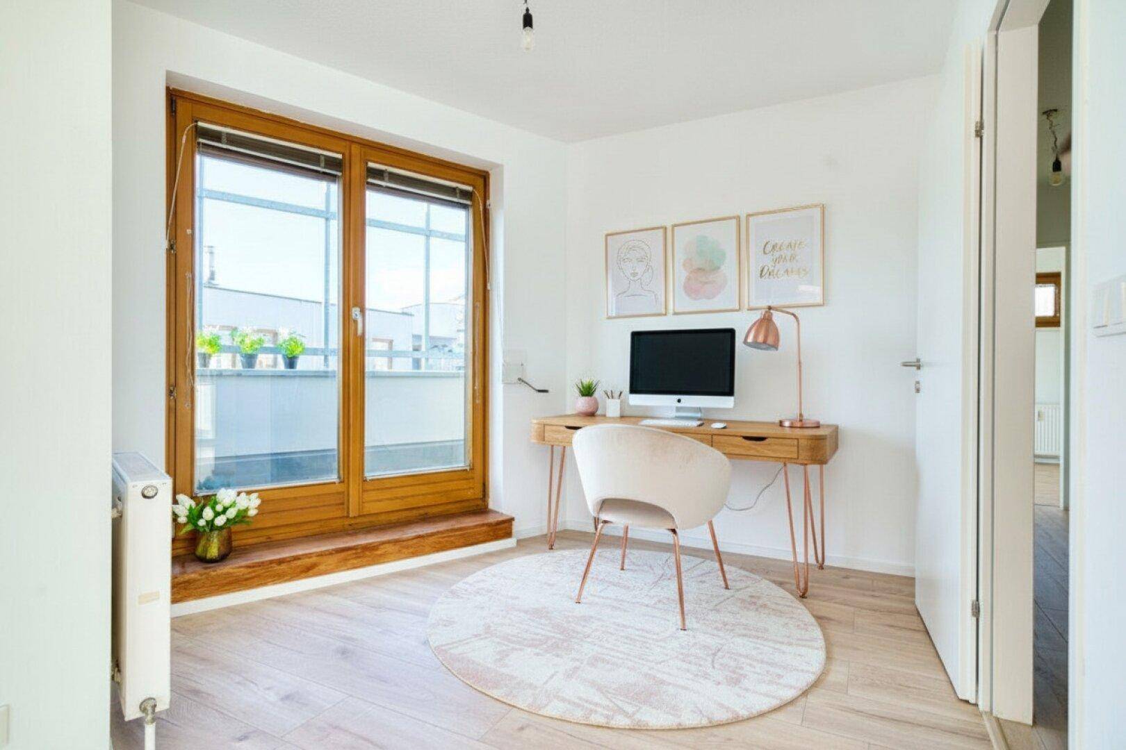 Modern eingerichtetes Büro mit Schreibtisch, Stuhl und viel Tageslicht durch große Fenster.