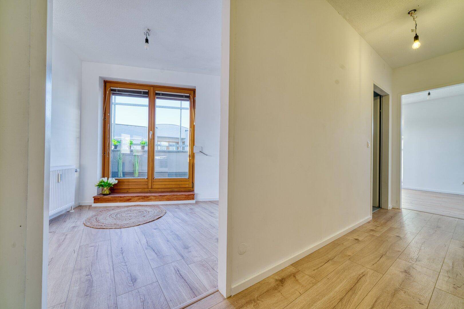 Heller Flur mit Holzboden, der zu weiteren Zimmern und einem Balkon führt.