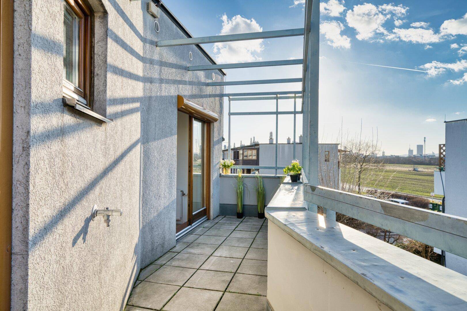 Sonniger Balkon mit Fliesenboden und Pergola-Struktur, bietet weiten Blick ins Grüne.