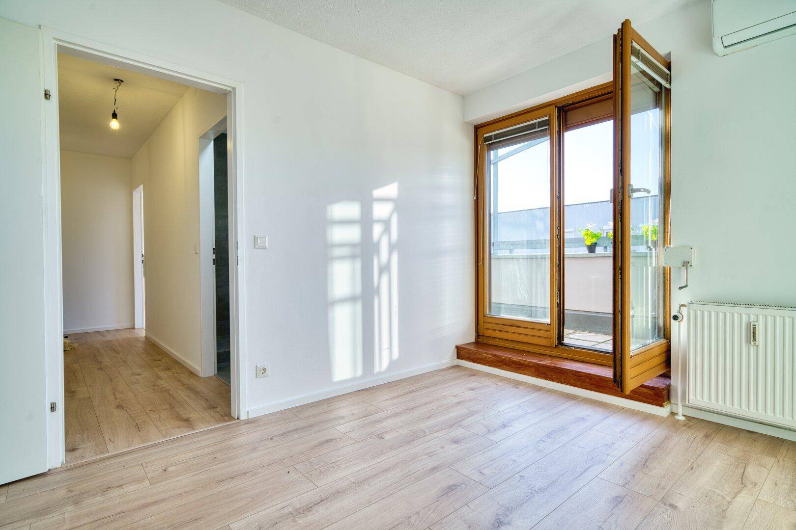 Geräumiges, helles Zimmer mit Holzboden und Zugang zu einem sonnigen Balkon.