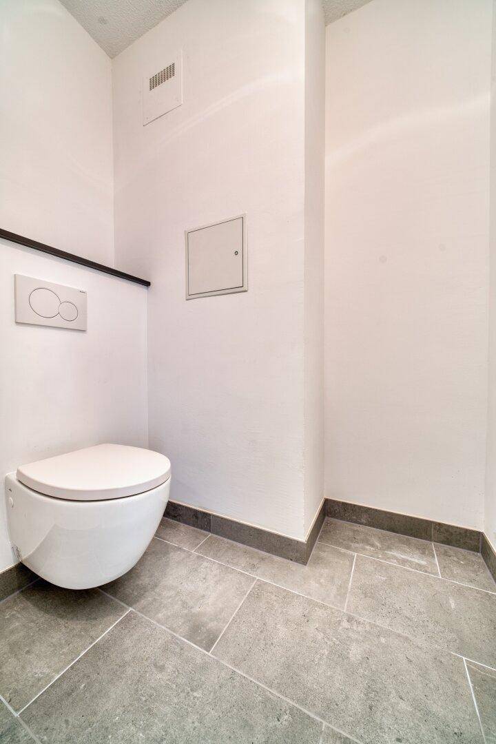 Separates Gäste-WC mit wandhängender Toilette und modernen grauen Fliesen.