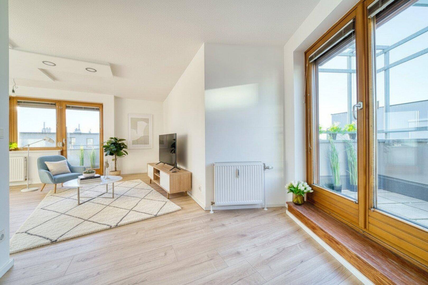 Gemütlicher Wohnbereich mit modernen Möbeln, Teppich und viel Tageslicht durch große Fenster.