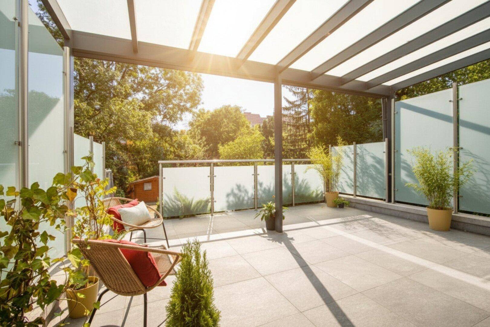 Sonnige Terrasse mit Pergola, Glaswänden und bequemen Outdoor-Sesseln, umgeben von Grün.