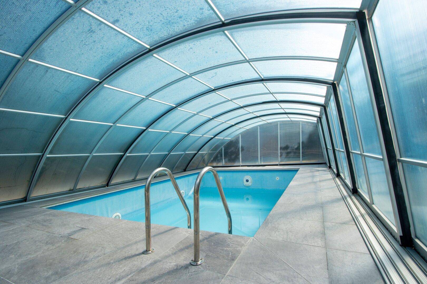 Überdachtes Schwimmbad mit blauen Fliesen und Zugangstreppe, ideal für alle Jahreszeiten.