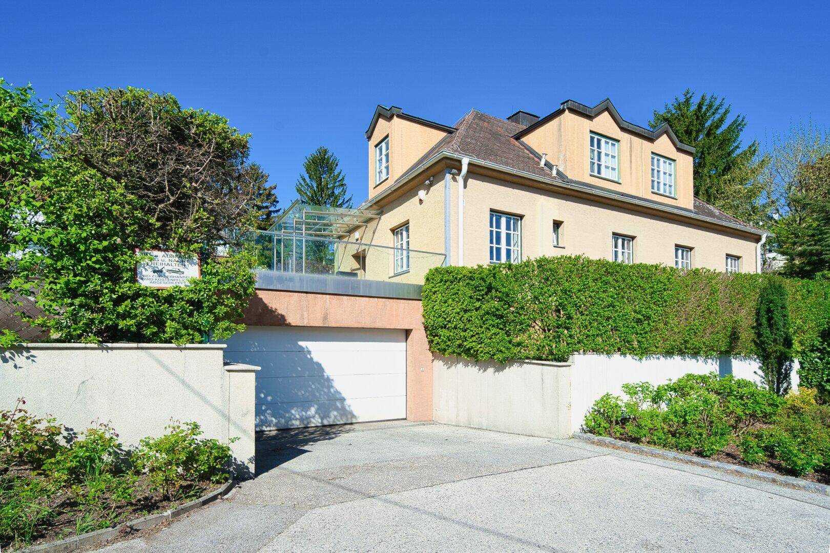 Ansicht des Hauses mit integrierter Garage, gepflegter Hecke und sonniger Einfahrt.
