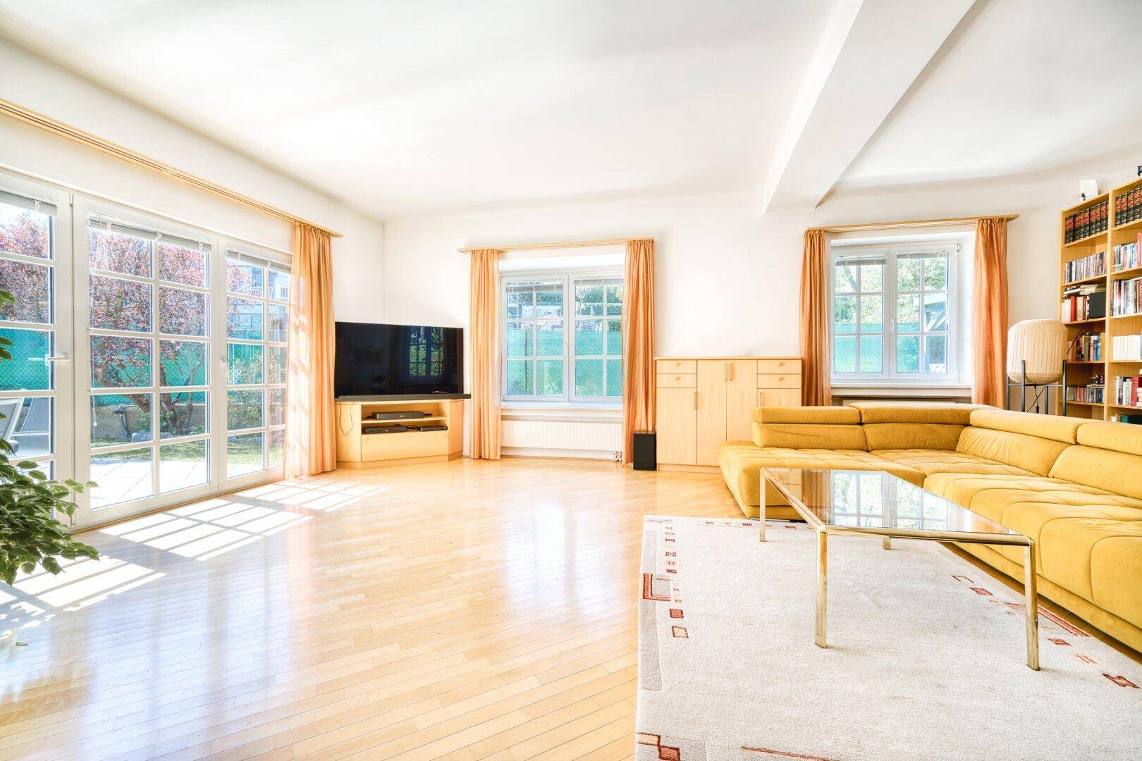 Helles Wohnzimmer mit Parkettboden, großer Fensterfront und gelbem Ecksofa.