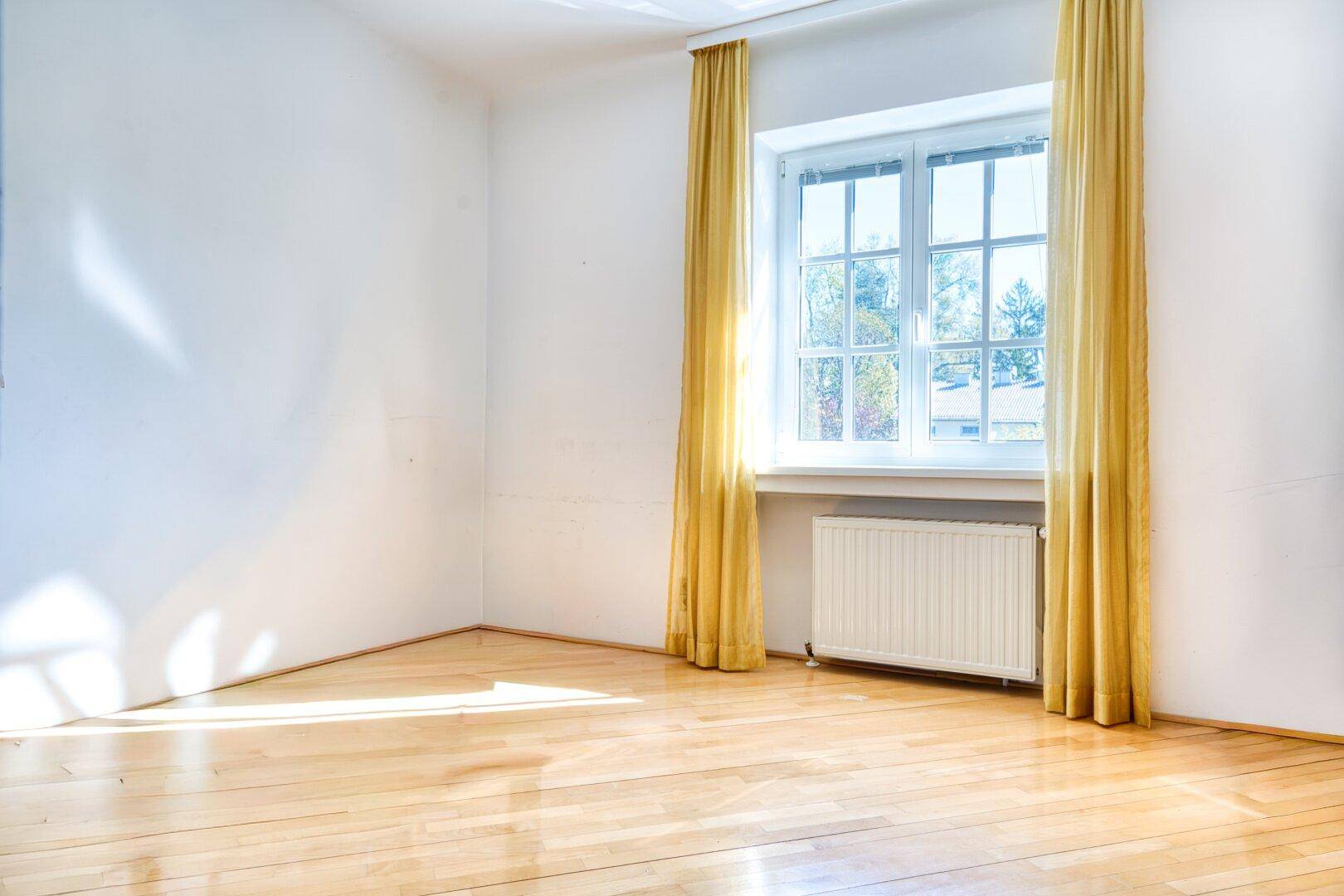 Helles Zimmer mit Parkettboden und großem Fenster, ideal als Schlaf- oder Arbeitszimmer.