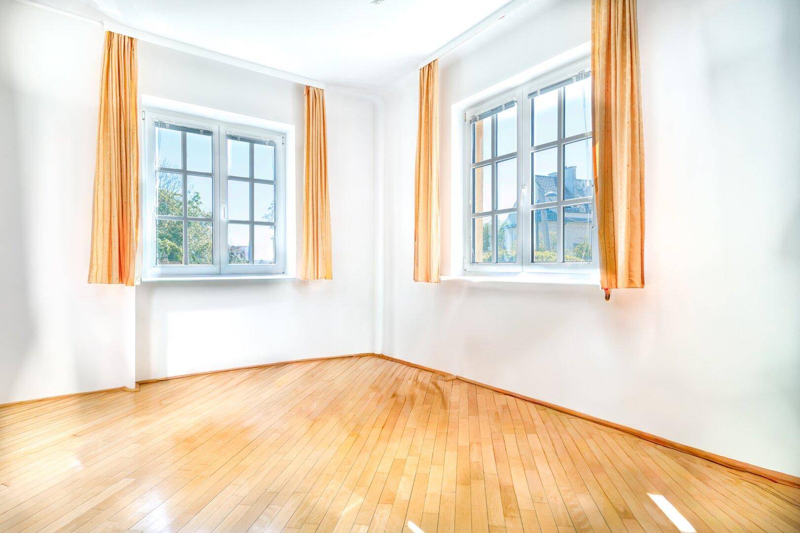 Lichtdurchflutetes Zimmer mit Parkettboden und zwei Fenstern, bereit zur individuellen Gestaltung.