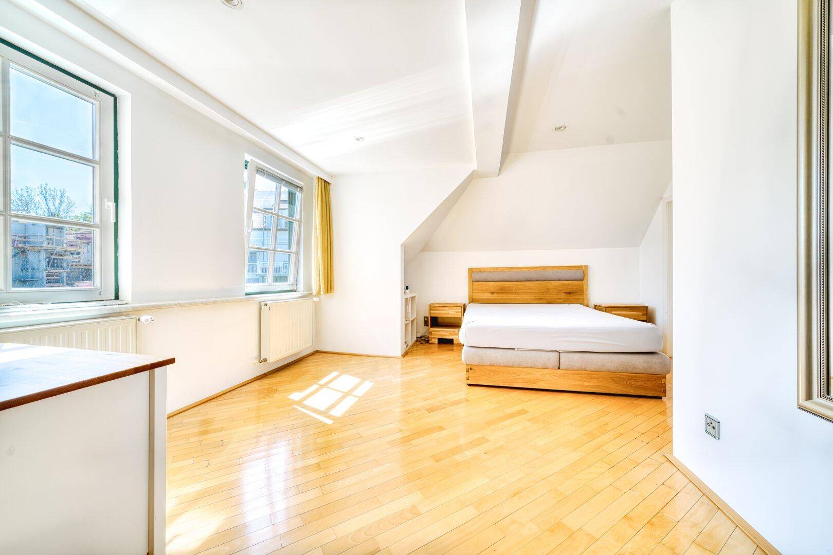 Geräumiges Schlafzimmer mit Parkettboden, Dachschrägen und viel natürlichem Licht.