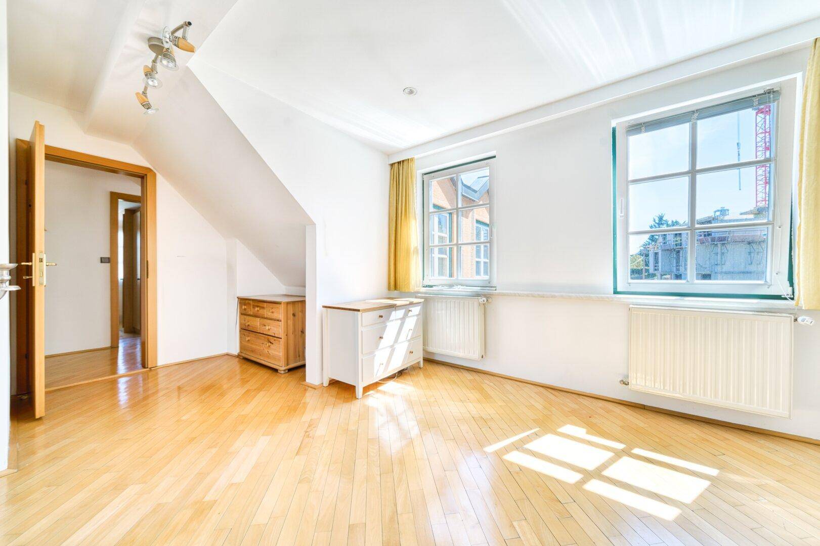 Helles Schlafzimmer mit Parkettboden, Dachschräge und zwei Fenstern für gute Belichtung.