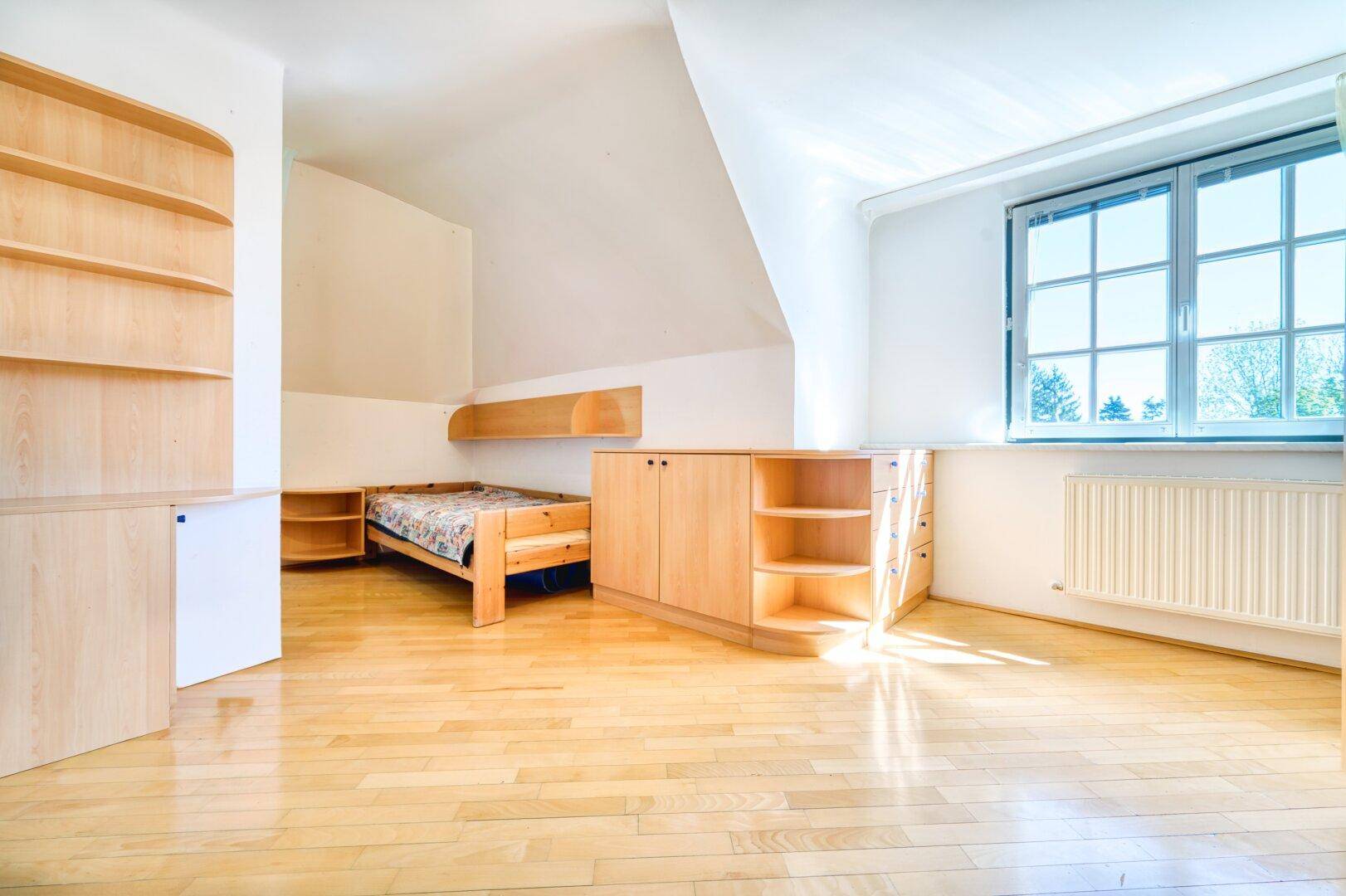 Schlafzimmer mit Parkettboden, Dachschräge und integrierten Holzmöbeln.