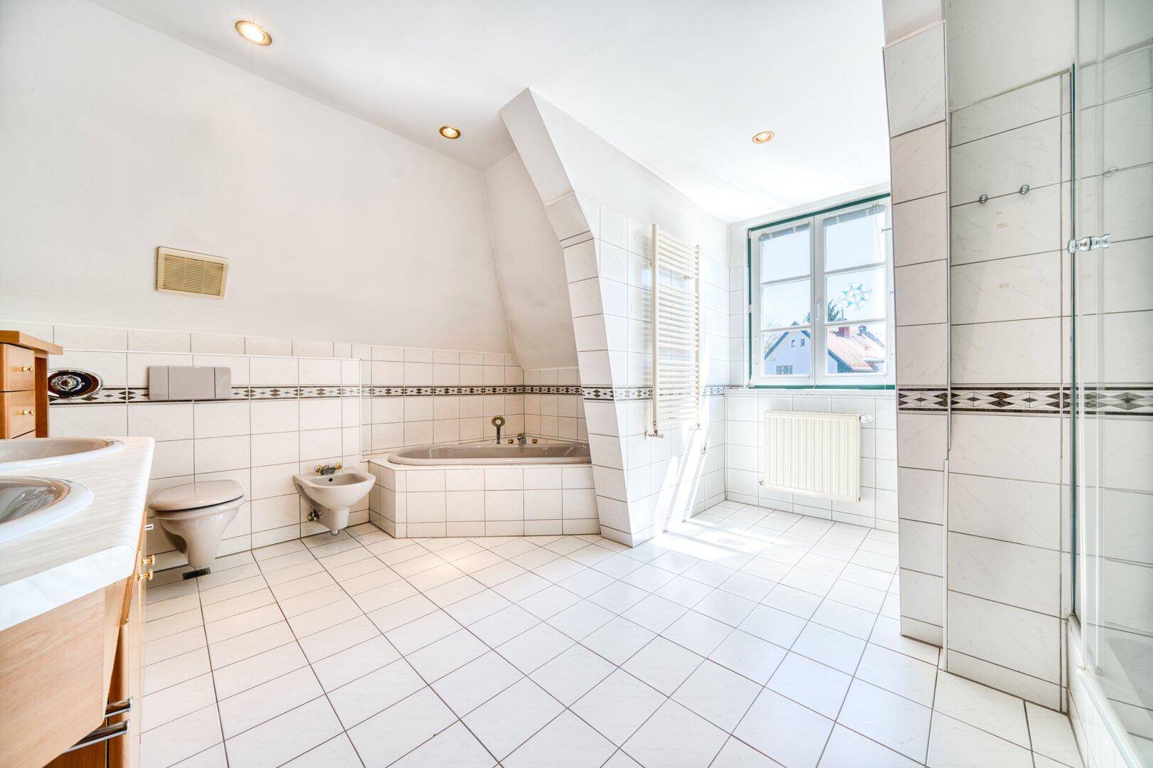 Geräumiges Badezimmer mit weißen Fliesen, Badewanne, Bidet und Dachschräge.