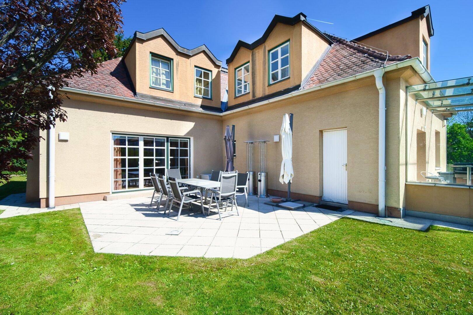 Große gepflasterte Terrasse mit Gartenmöbeln und Zugang zum Rasenbereich.