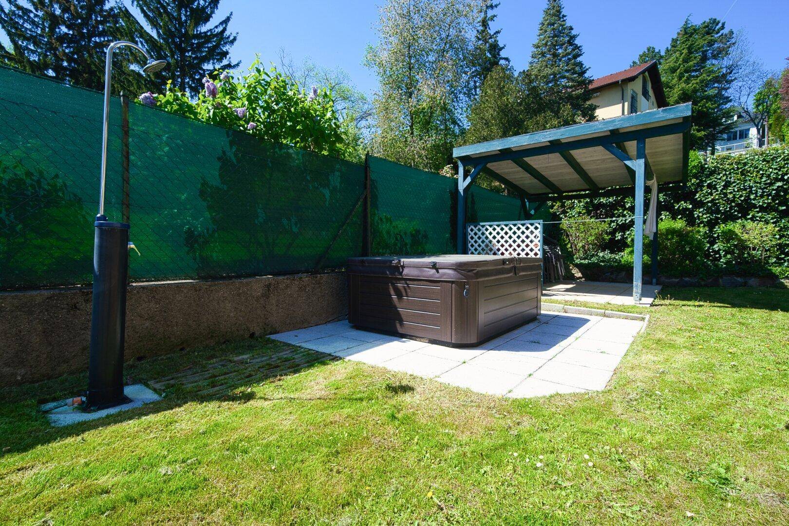 Gartenbereich mit Whirlpool und Außendusche unter einem schattenspendenden Unterstand.