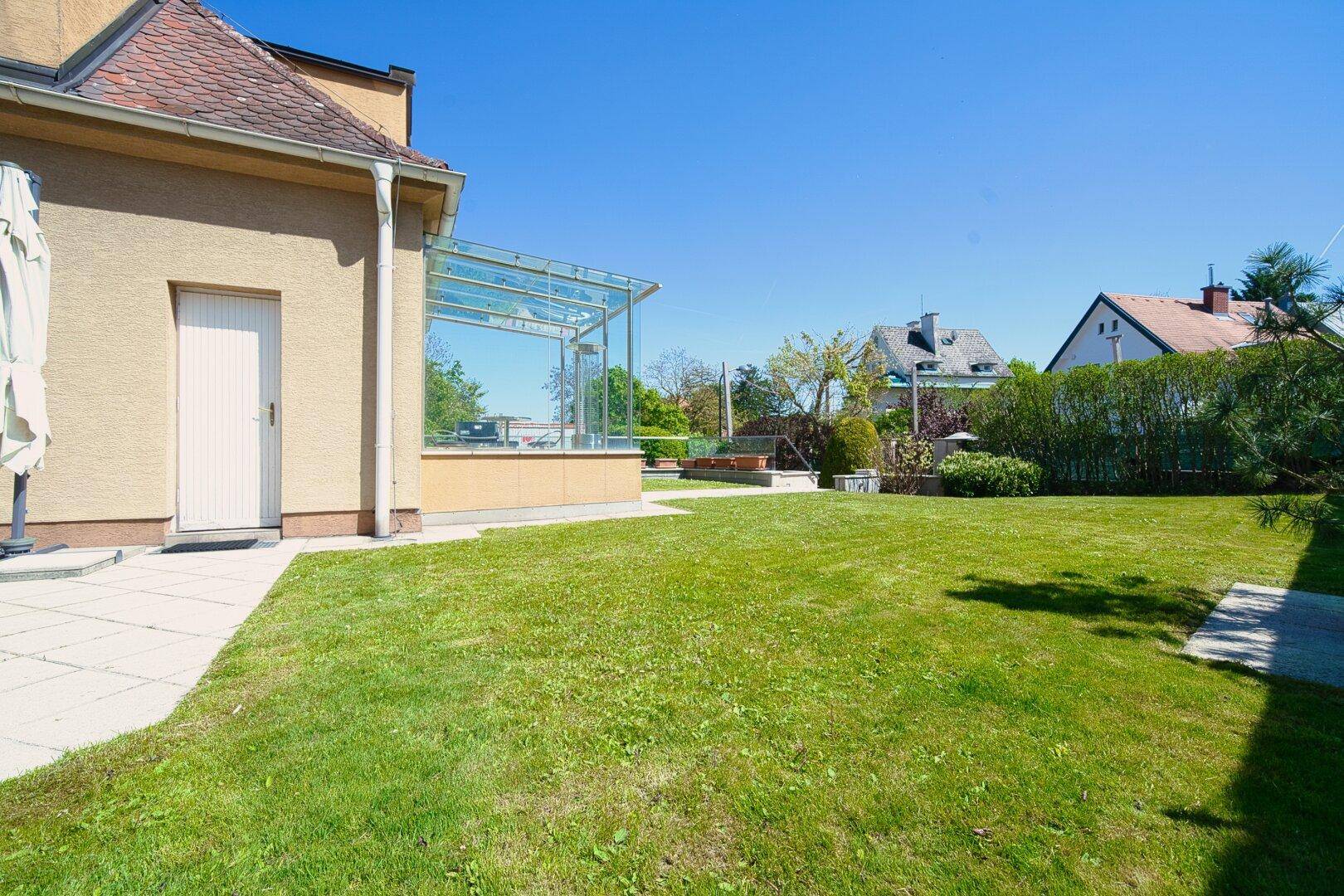 Weitläufiger Garten mit Rasenfläche und Zugang zur Terrasse und zum Wintergarten.