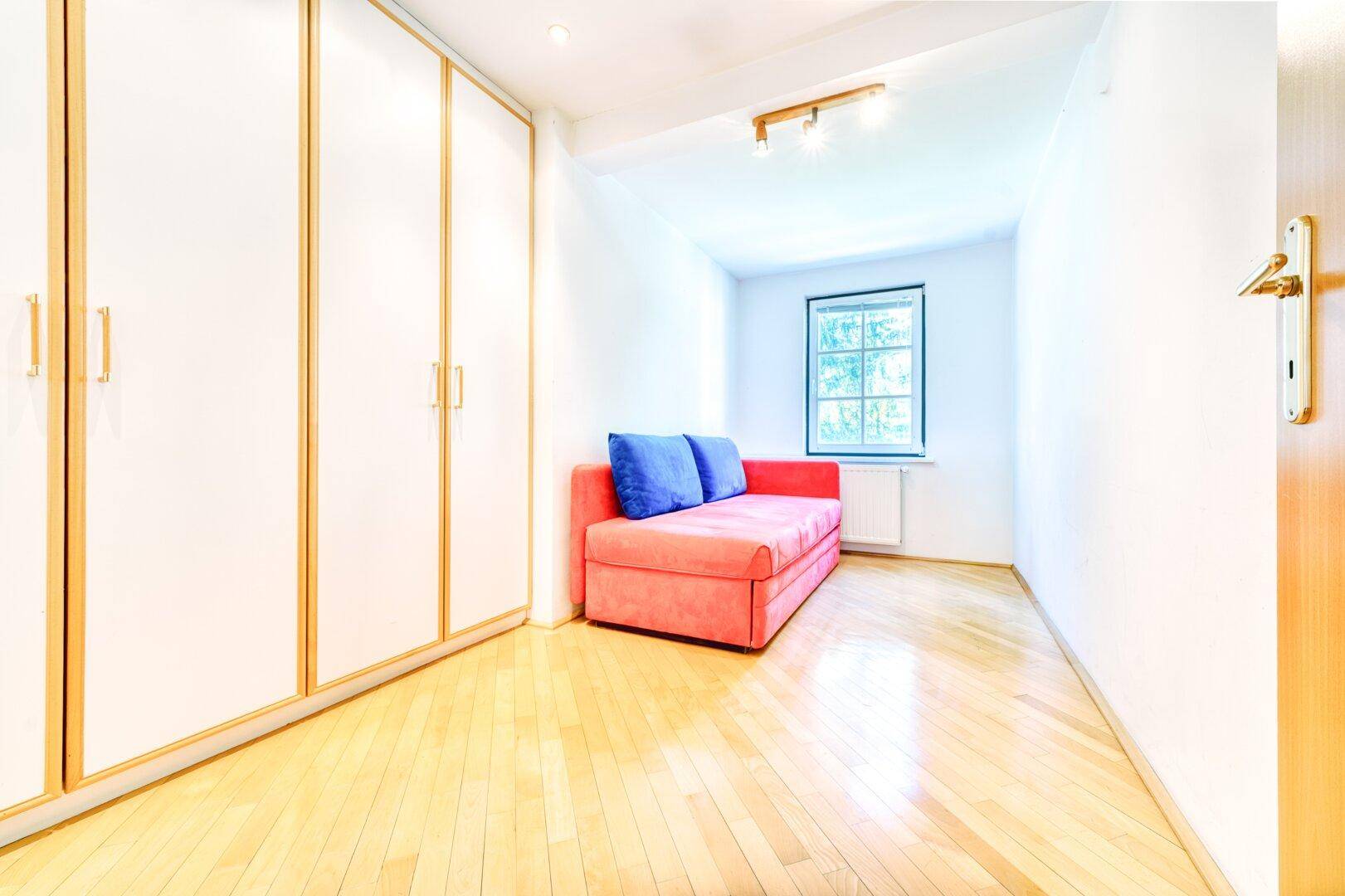 Kleines Zimmer mit Parkettboden, Einbauschränken und einem Schlafsofa.