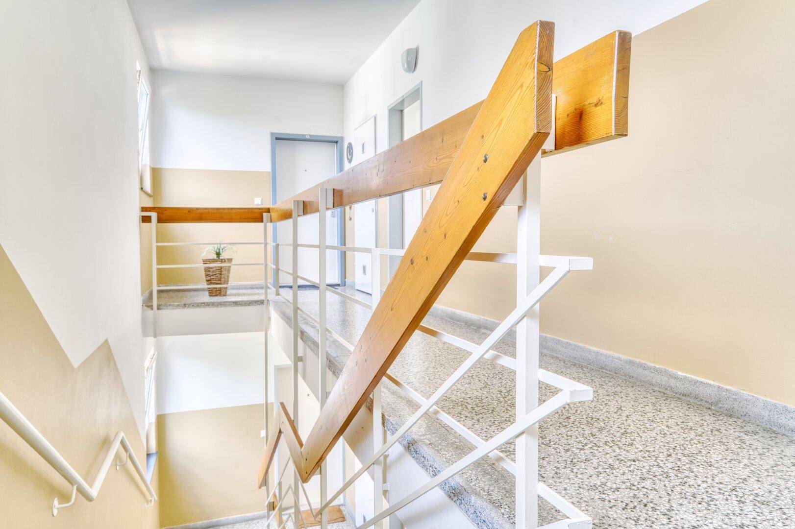 Treppenhaus mit Holzgeländer und Terrazzoboden in einem Mehrfamilienhaus, gut gepflegt.