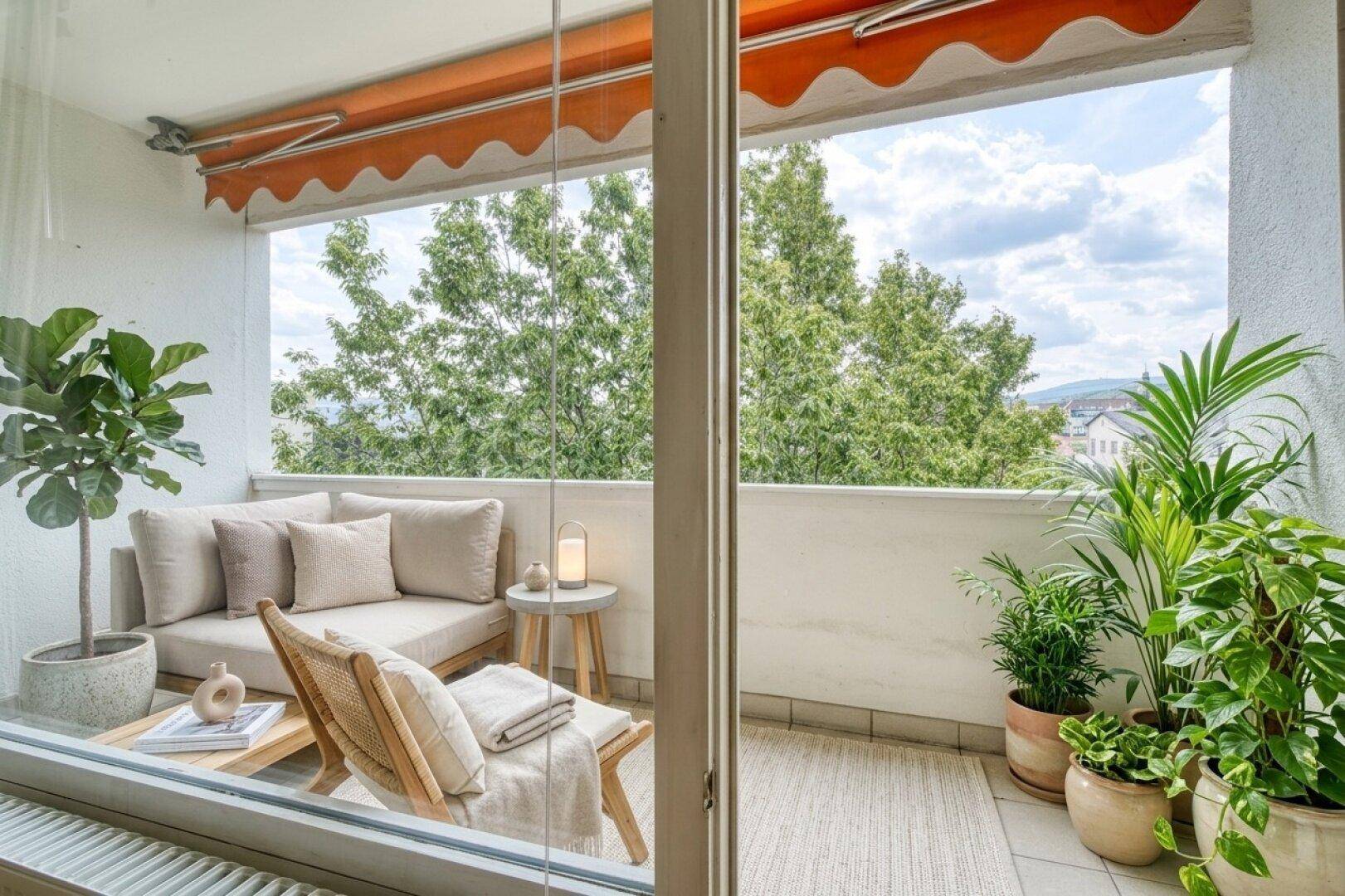 Möblierter Balkon mit bequemen Sitzgelegenheiten, vielen Pflanzen und Blick ins Grüne.