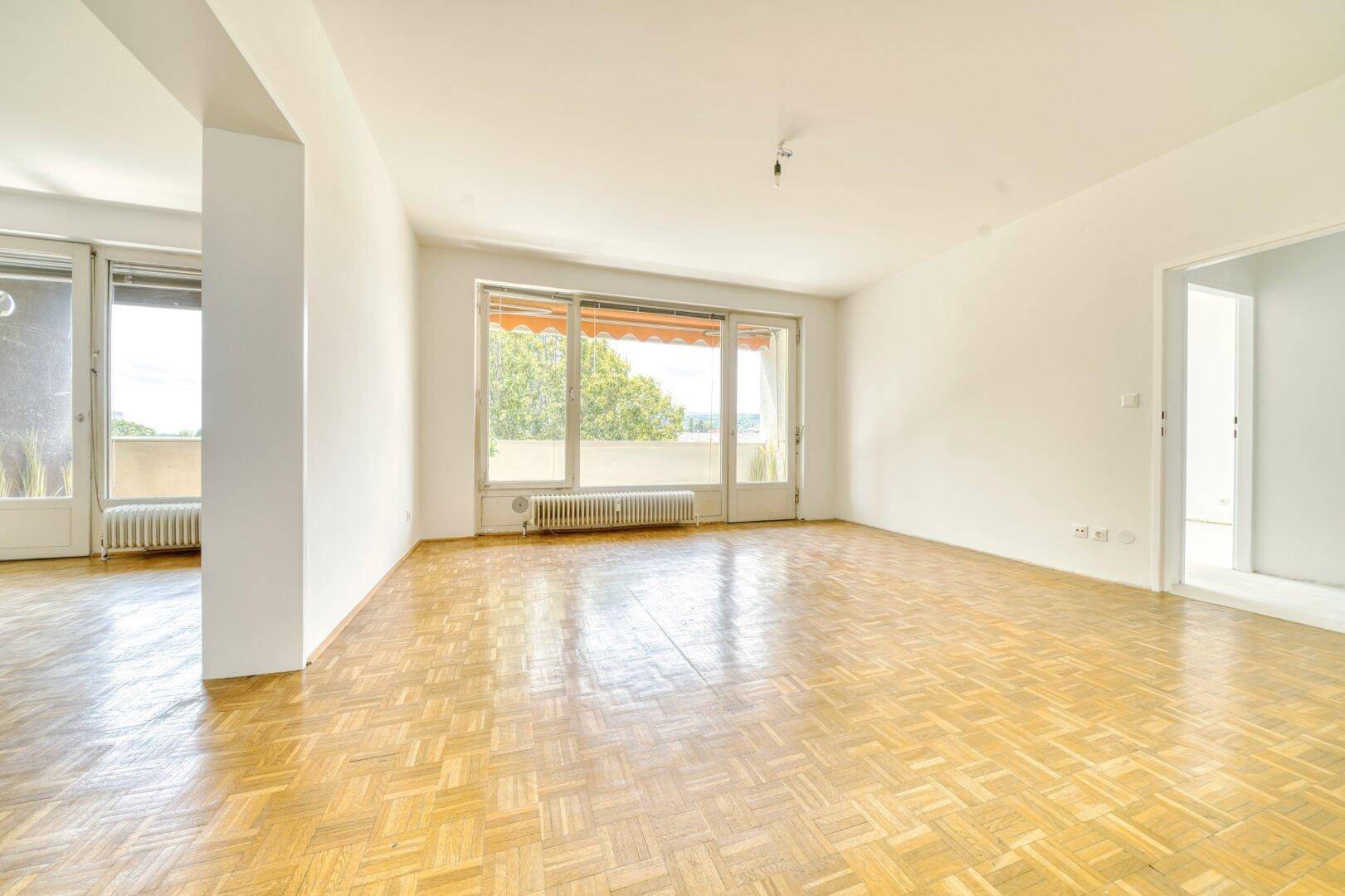 Geräumiges Wohnzimmer mit hellem Parkettboden und viel Tageslicht durch die Balkontür.