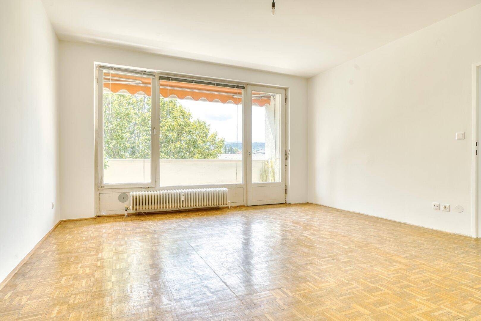 Lichtdurchflutetes Wohnzimmer mit Parkettboden und direktem Zugang zum Außenbereich.