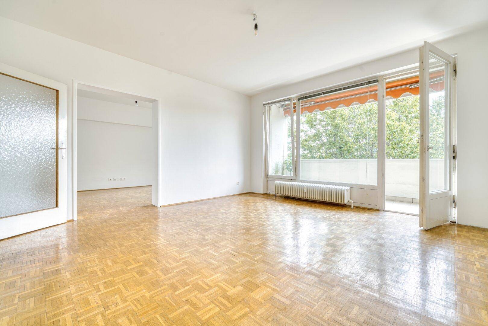 Helles Wohnzimmer mit Fischgrätparkett und Zugang zu einem sonnigen Balkon.