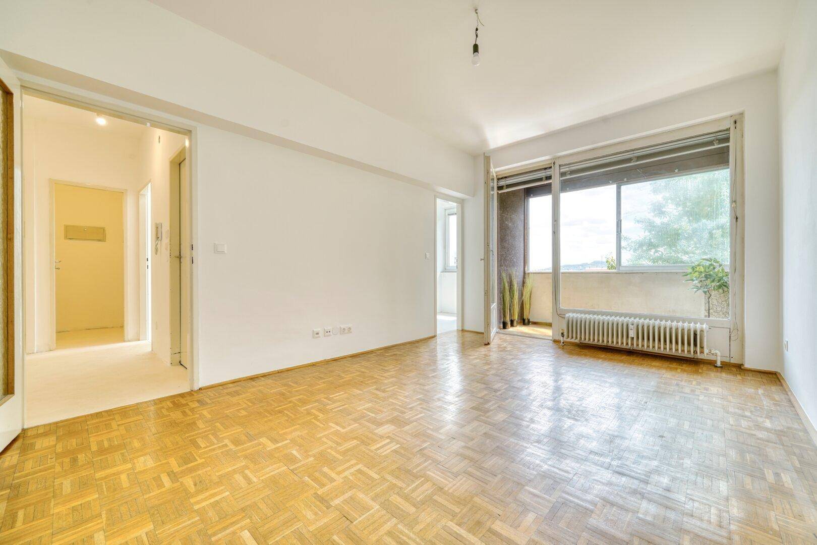 Helles Wohnzimmer mit Parkettboden und Schiebetür zum Balkon.