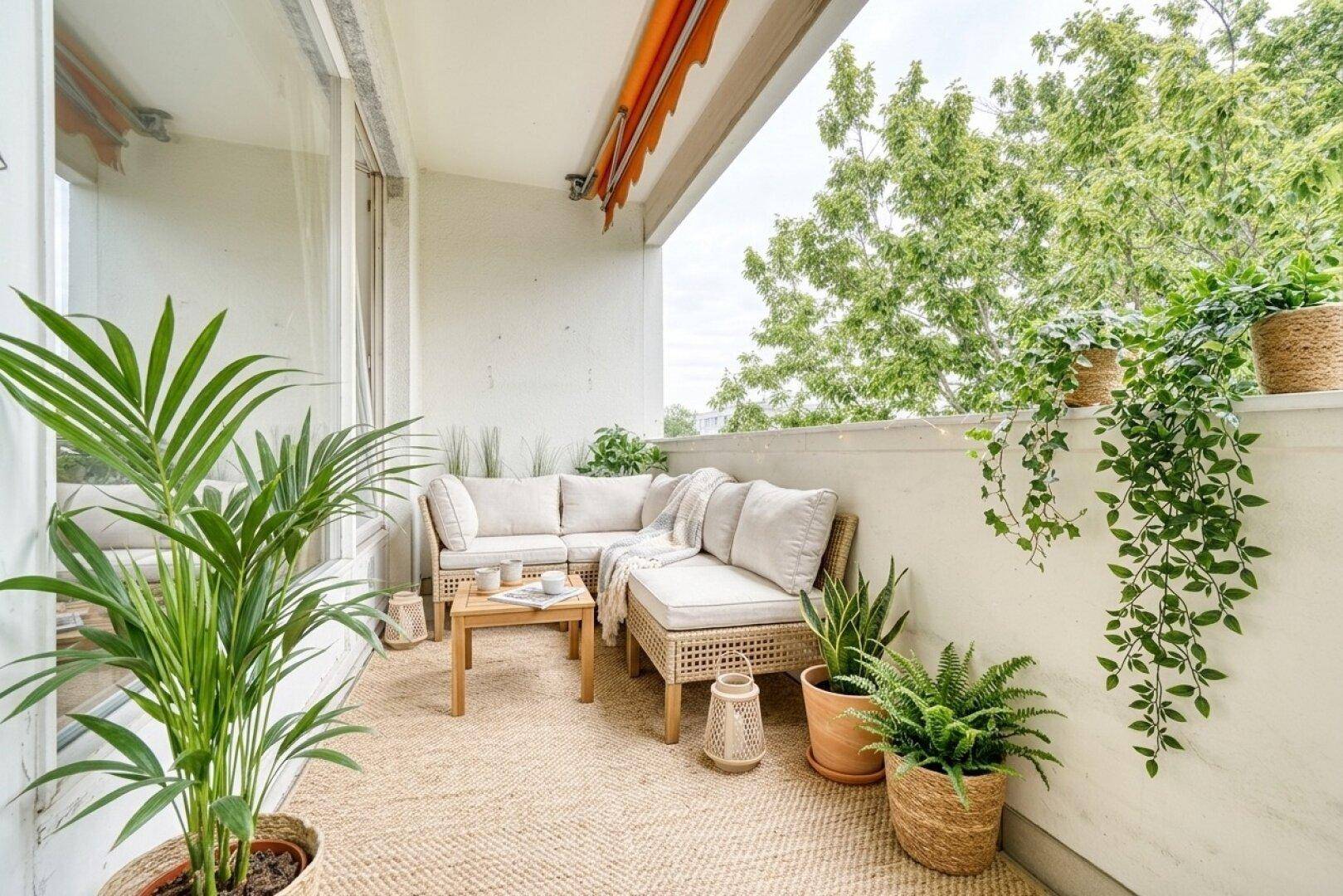 Gemütlicher Balkon mit Rattanmöbeln, vielen Pflanzen und Blick ins Grüne.