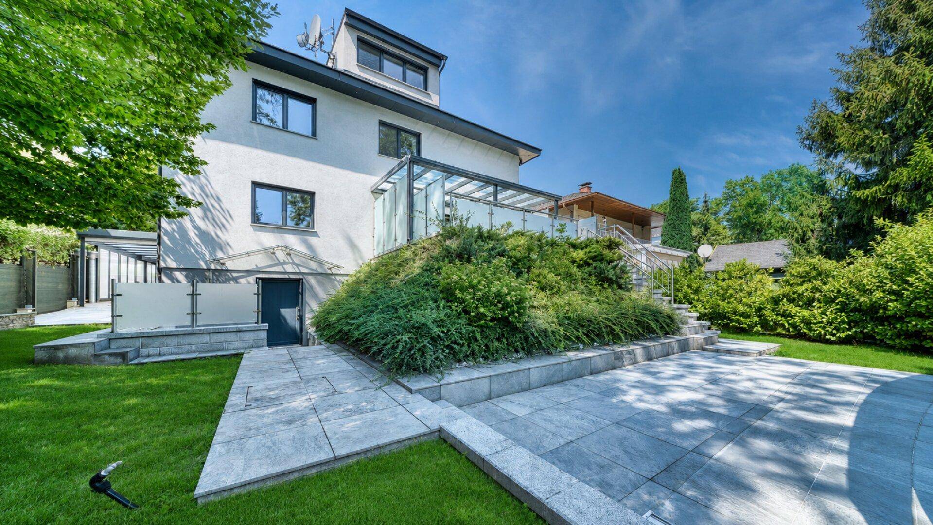 Rückseite des Hauses mit gepflegtem Garten, Terrassenbereich und Zugang zum Keller.