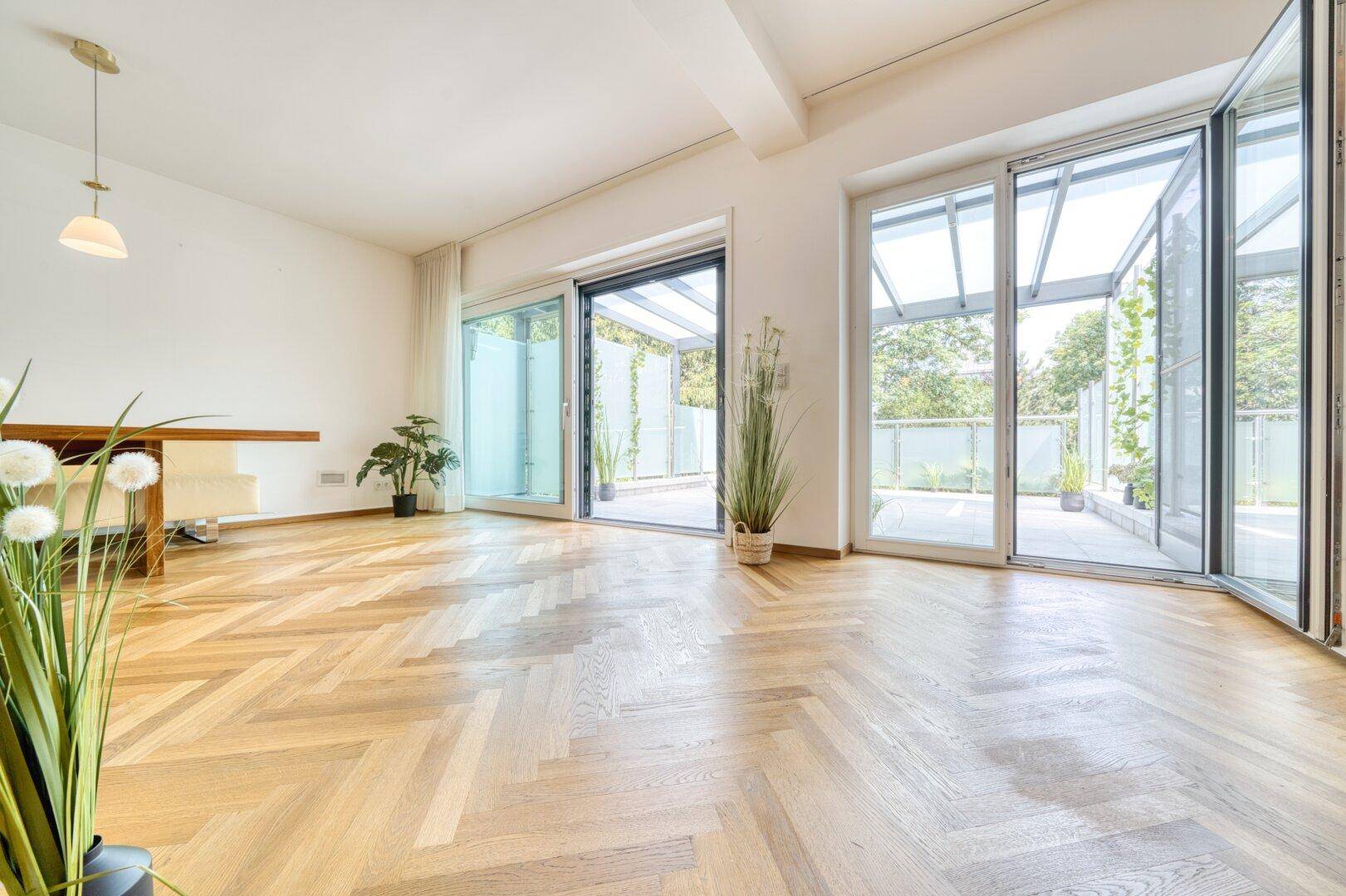 Helles Wohnzimmer mit großen Glasfronten und Zugang zu einer überdachten Terrasse.