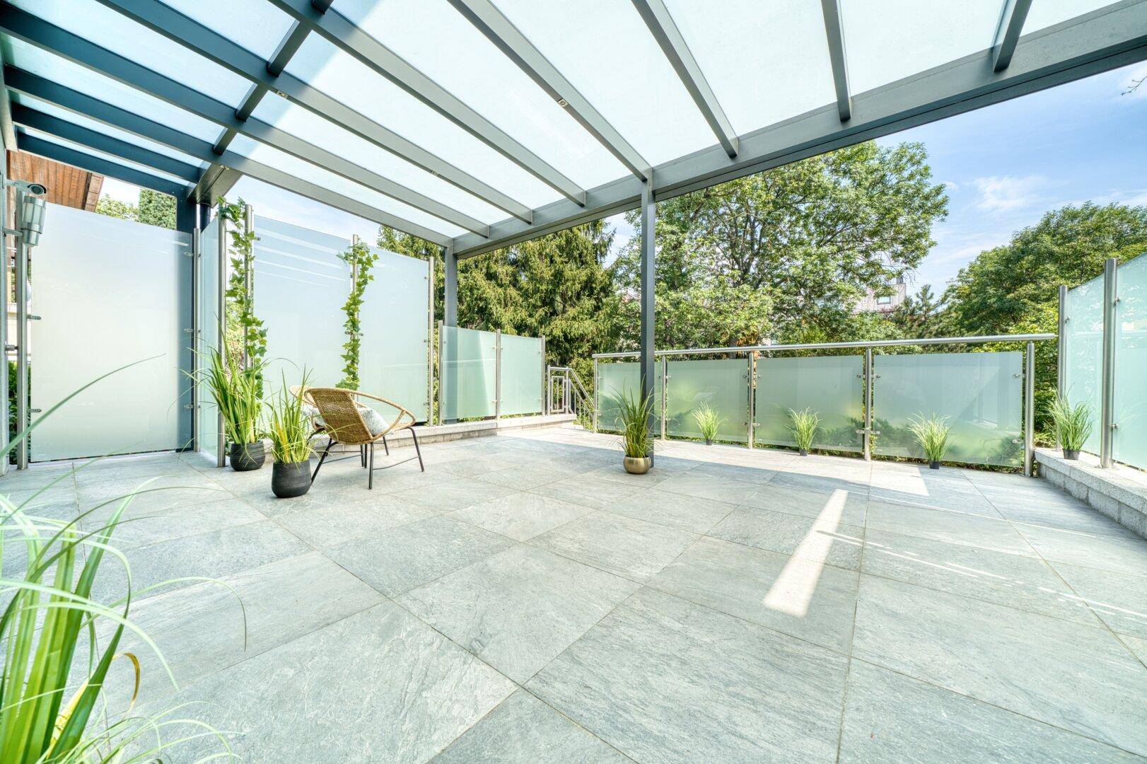 Großzügige, überdachte Terrasse mit modernen Glaswänden und Sitzgelegenheiten.
