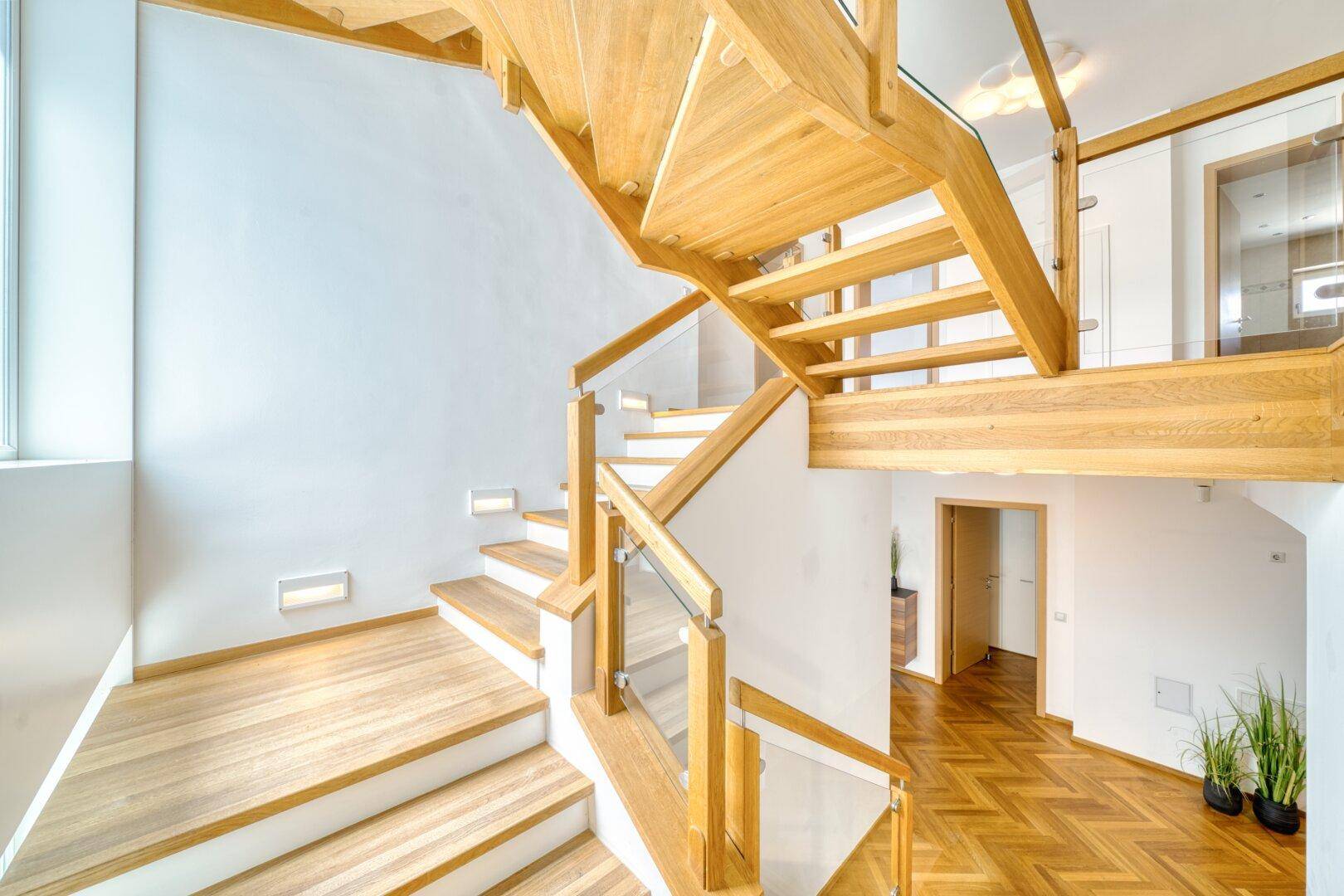 Elegante Holztreppe mit Glasgeländer, die die verschiedenen Ebenen verbindet.