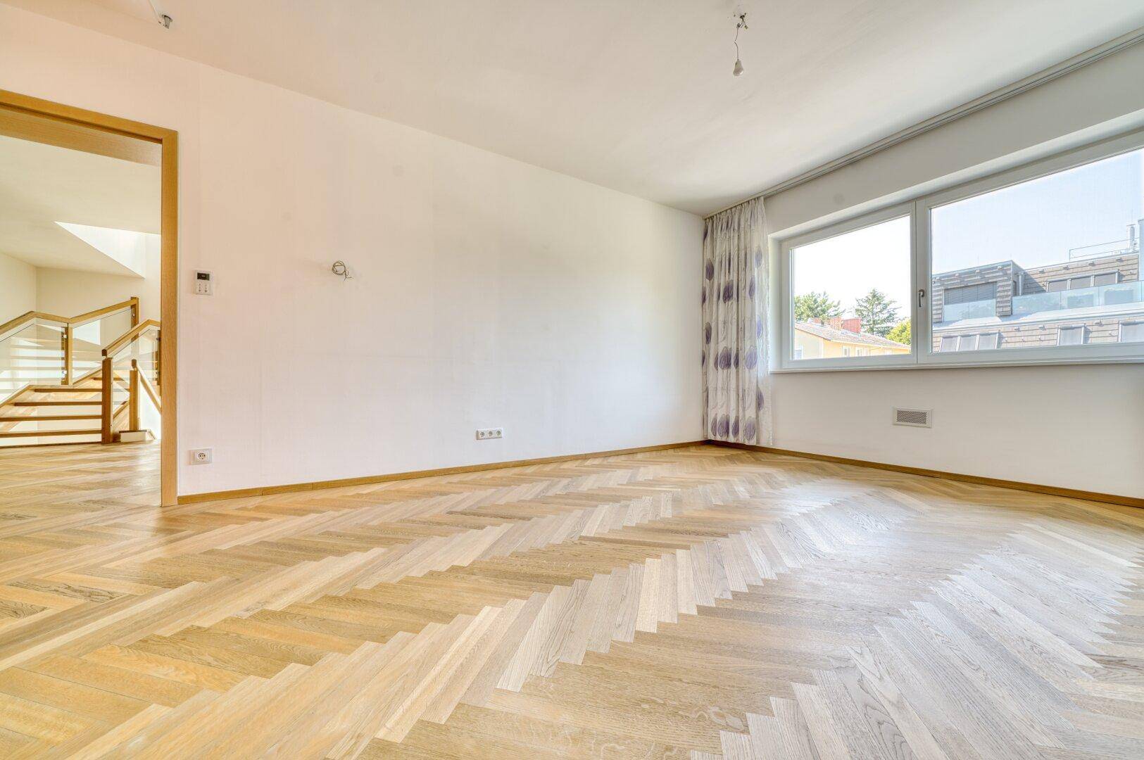 Helles Zimmer mit Fischgrätparkett und großem Fenster, ideal als Schlaf- oder Arbeitszimmer.