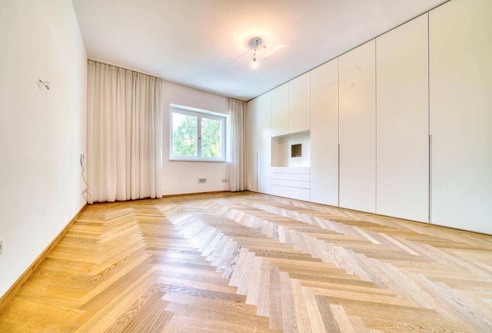 Schlafzimmer mit Fischgrätparkett und raumhohen Einbauschränken.