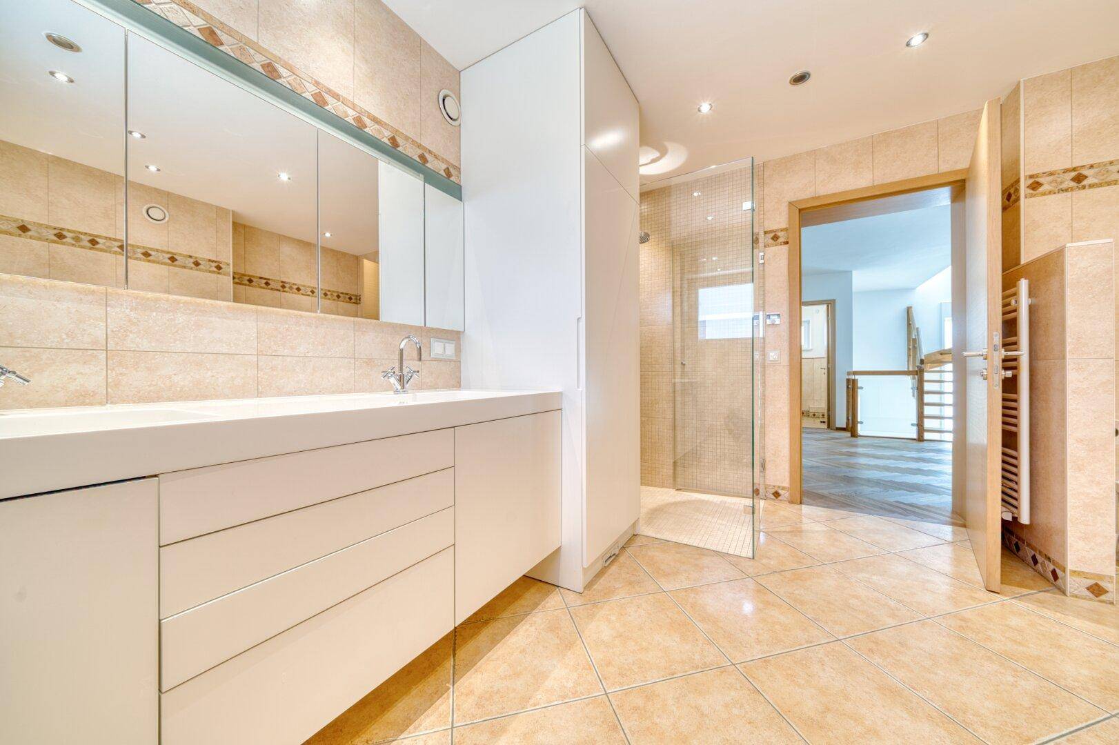 Modernes Badezimmer mit beigen Fliesen, großem Waschtisch und begehbarer Dusche.