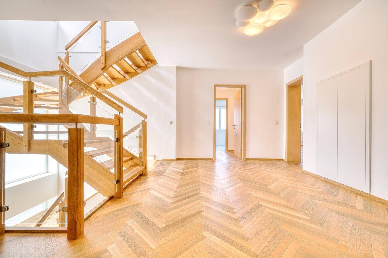 Heller Flur mit eleganter Holztreppe und Fischgrätparkett.