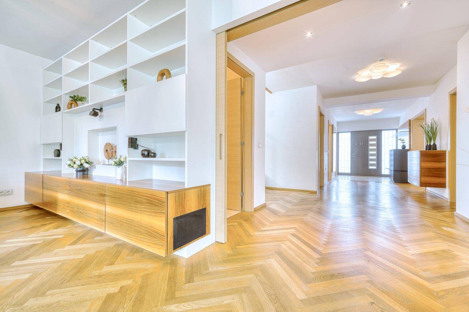 Offener Wohnbereich mit Fischgrätparkett, Einbauregalen und Blick zum Eingang.